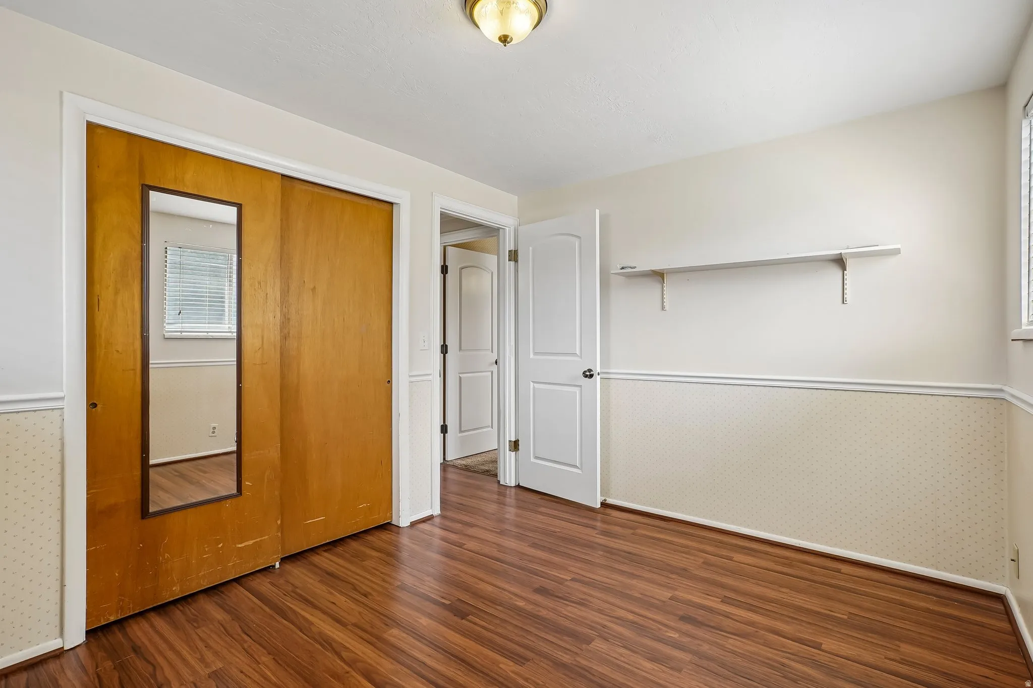 Room featuring wood-finish flooring, half-wall wainscoting, and a built-in wall shelf