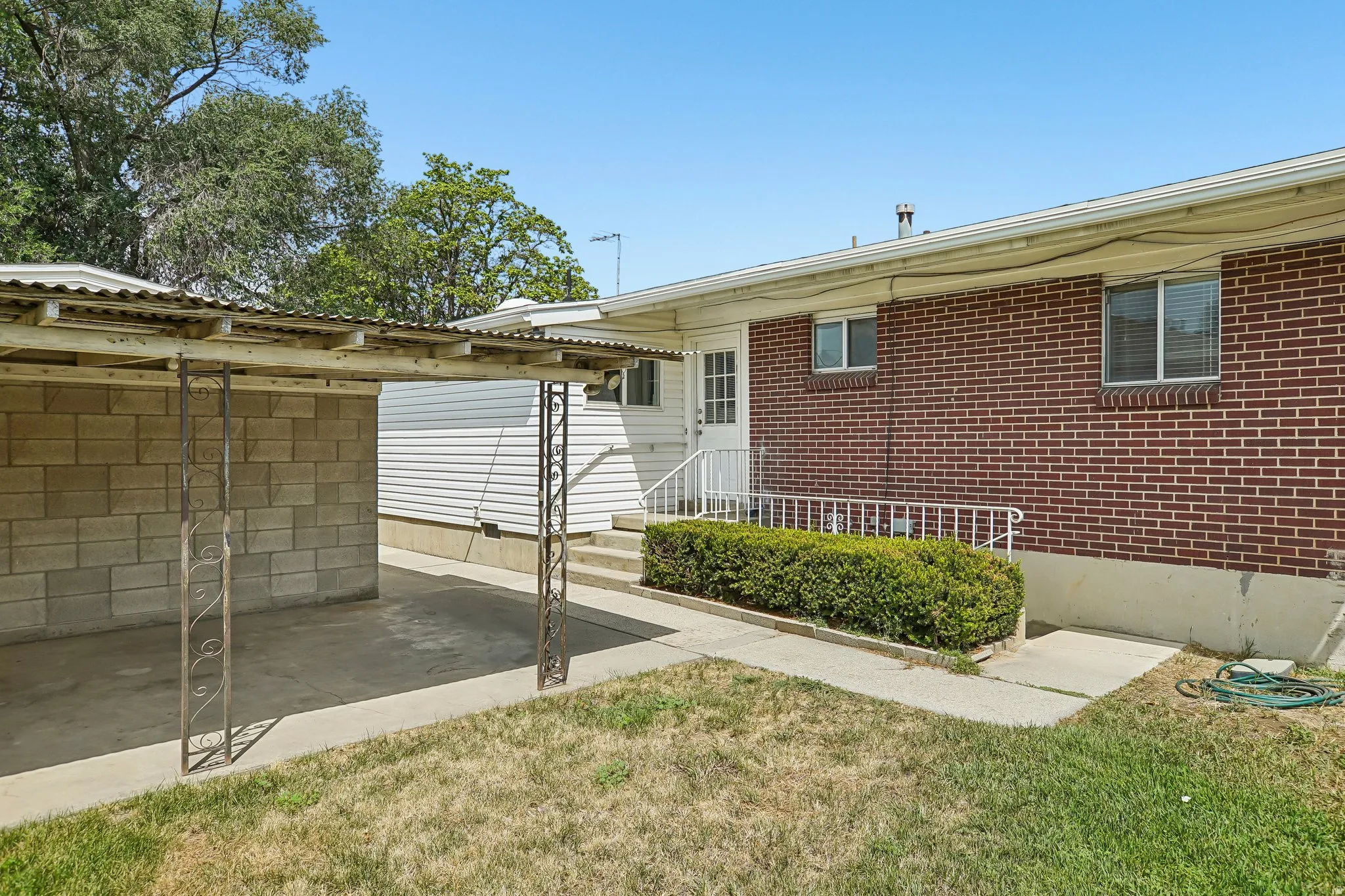 Red brick exterior with white trim windows and a covered carport featuring decorative wrought iron supports and a corrugated metal roof