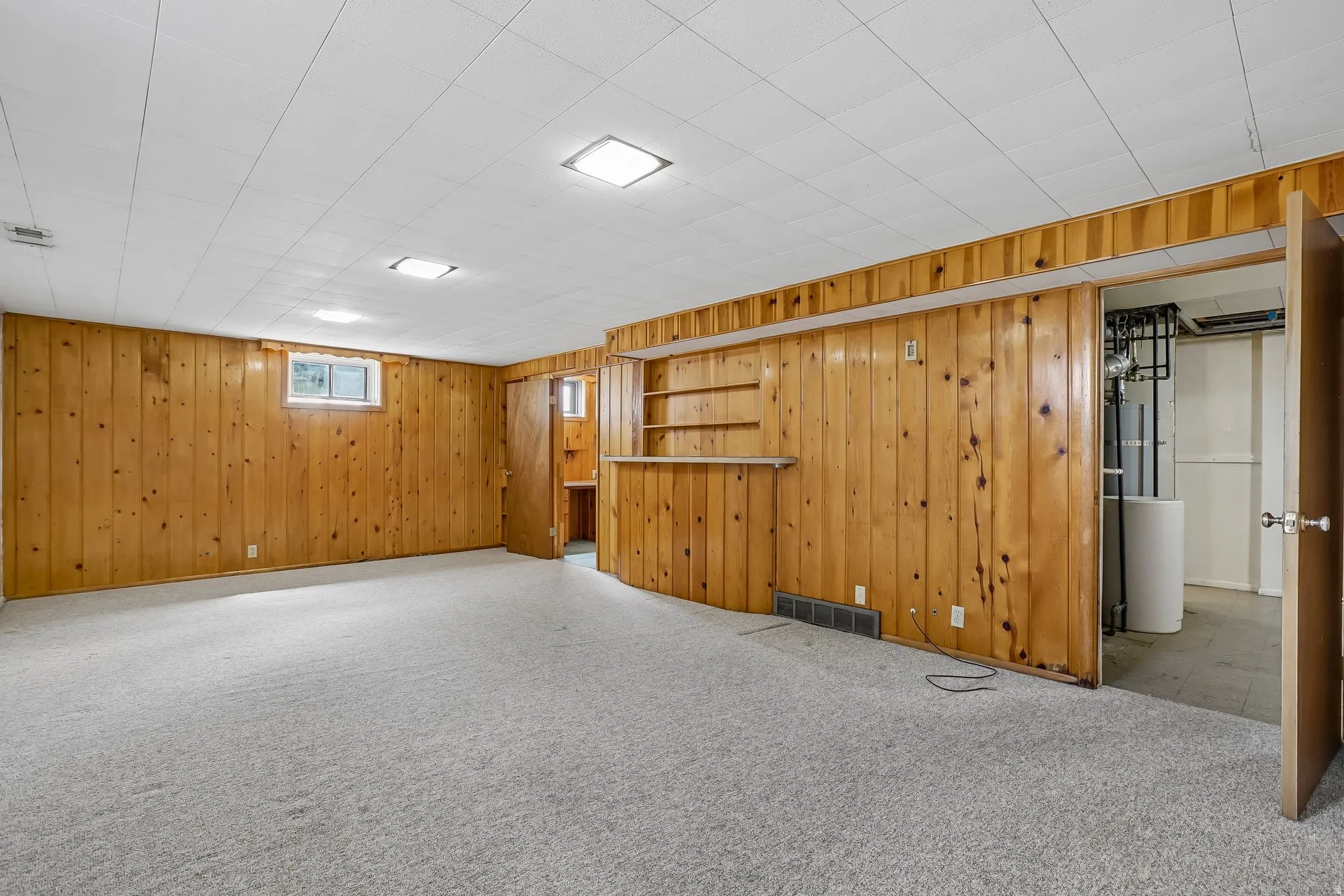 Finished room featuring wood-paneled walls, light-toned carpeting, and a built-in bar area with shelving