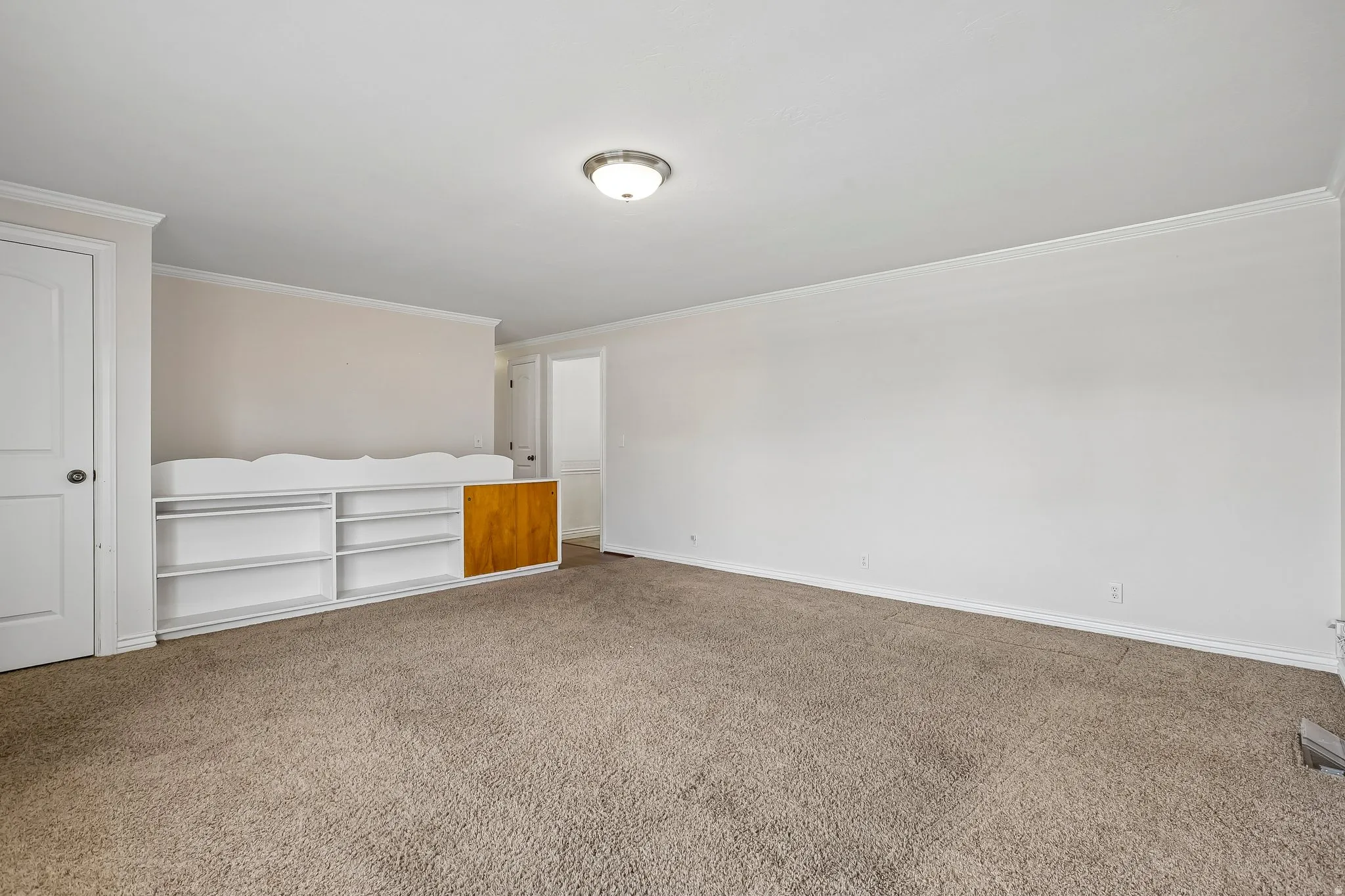 Spacious room featuring neutral carpeting and a built-in shelving unit with a wood-finish cabinet