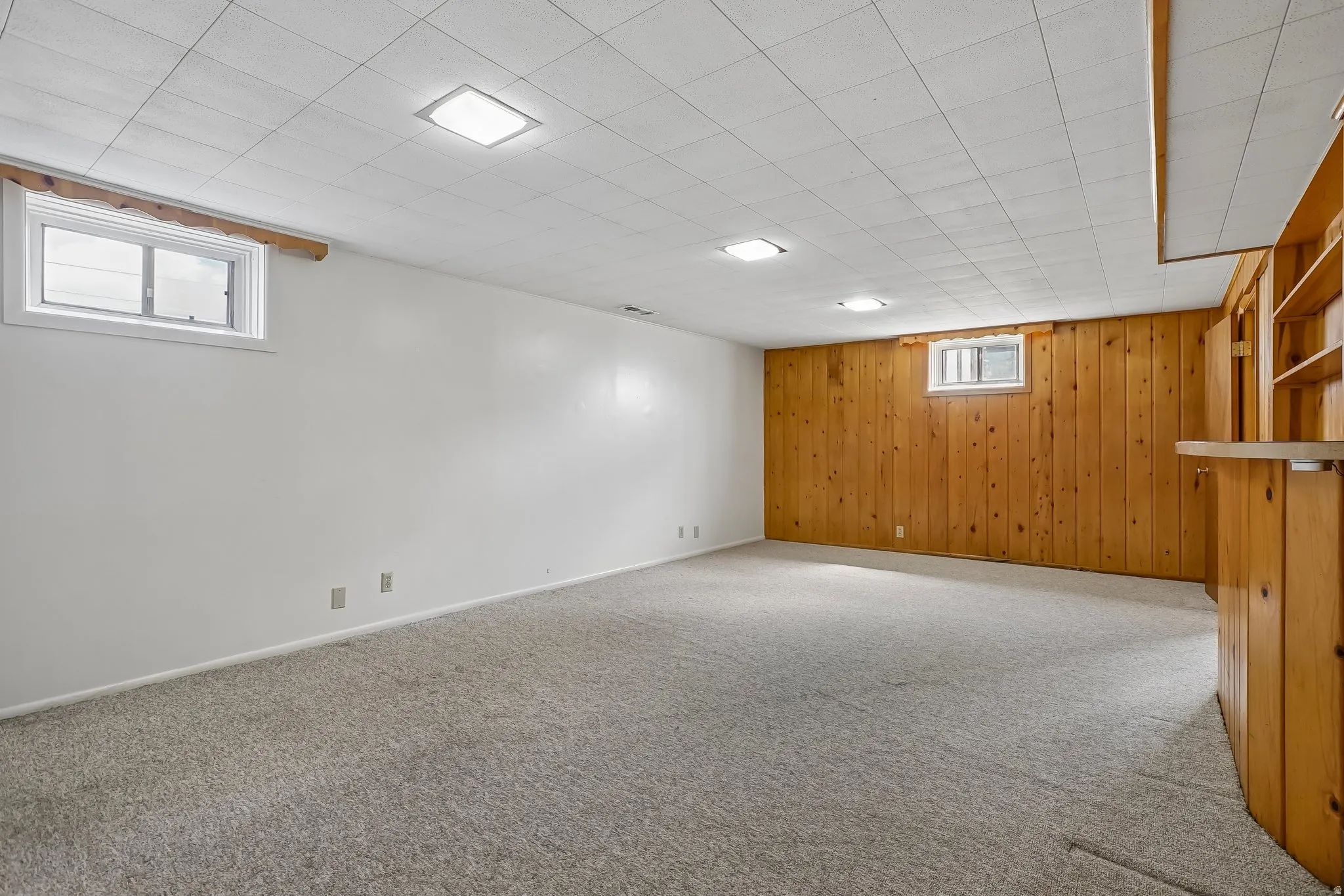 Carpeted room featuring a drop ceiling with recessed lighting, white painted walls, and wood-paneled accents