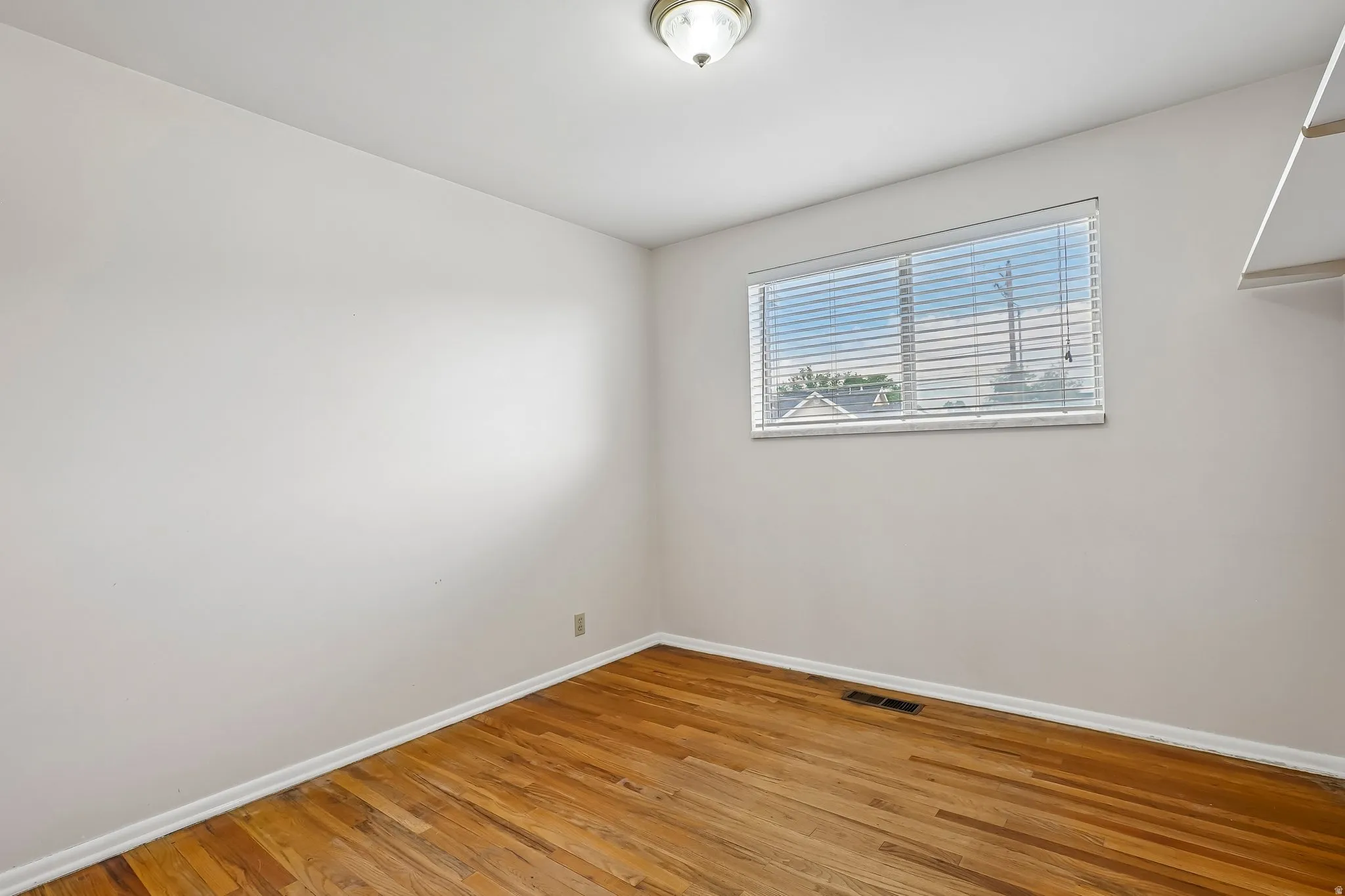 Room featuring wood-finish flooring, a window with horizontal blinds, and a flush mount ceiling light fixture