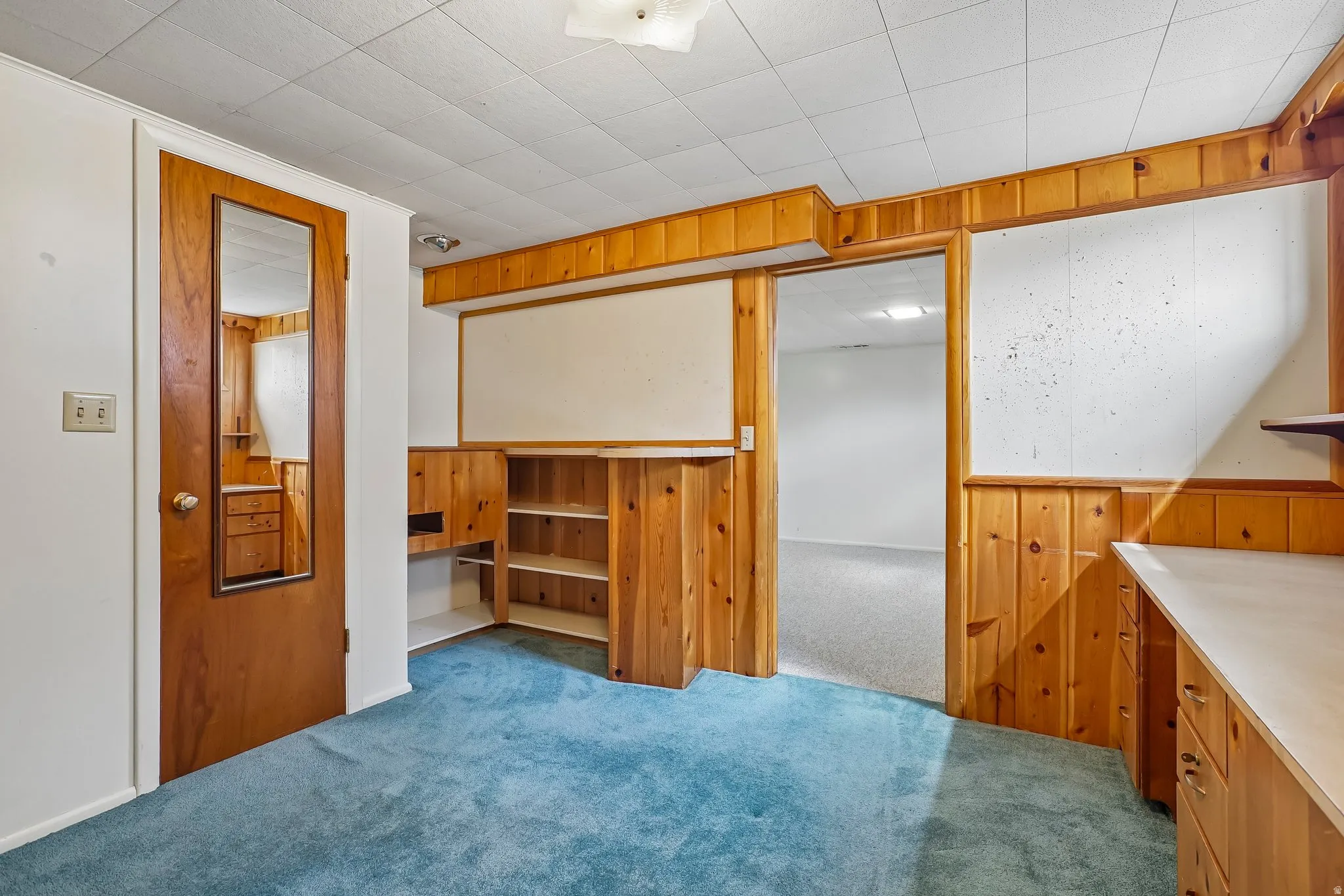 Room featuring wood paneling, built-in shelving, blue carpeting, and a drop ceiling