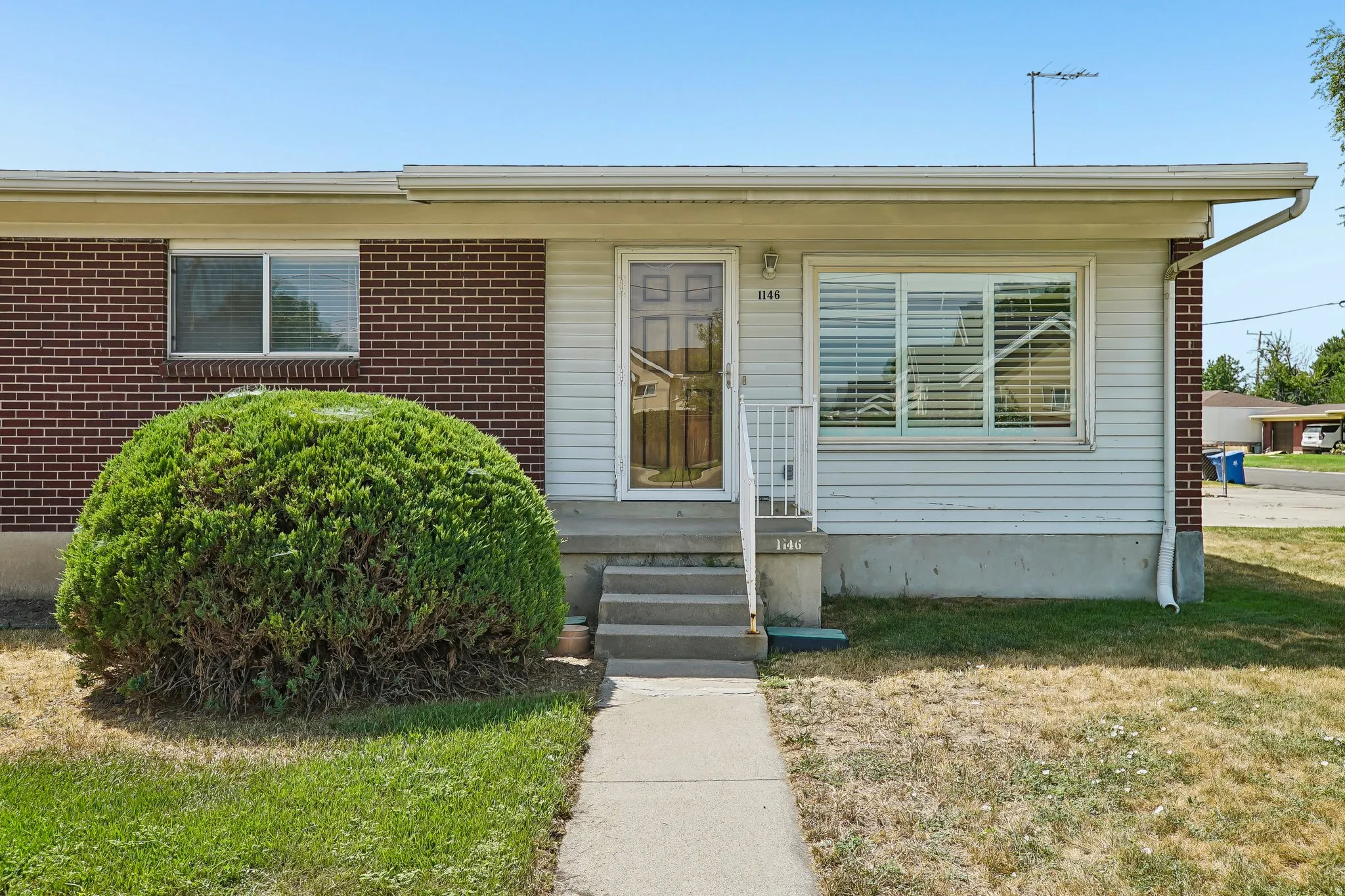 Brick and siding exterior featuring a concrete walkway, front porch with railing, and a mature shrub