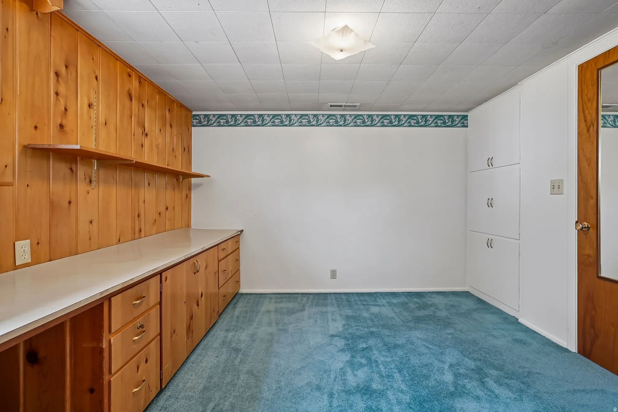 Room featuring extensive built-in wooden cabinetry with a light-toned countertop, coordinating wood paneling, and open shelving