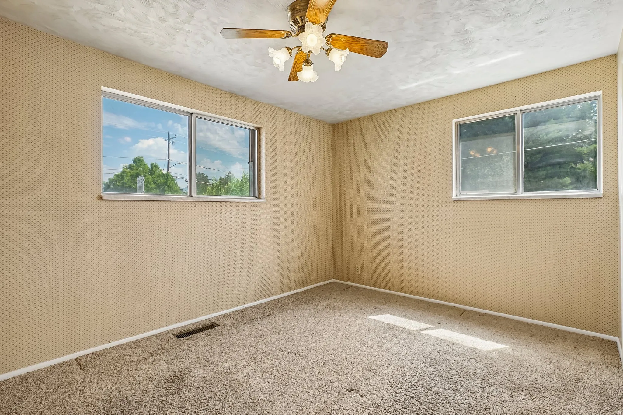 Carpeted room featuring dual windows, a textured ceiling, a ceiling fan with integrated lighting, and patterned wallpaper