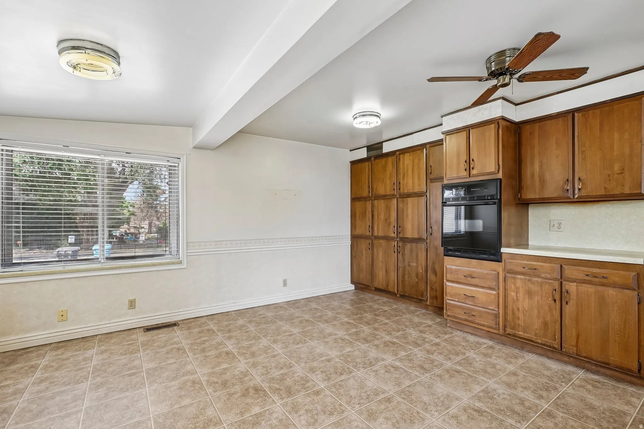 Kitchen space featuring tile flooring, wood cabinetry, built-in oven, solid surface countertops, and a ceiling fan