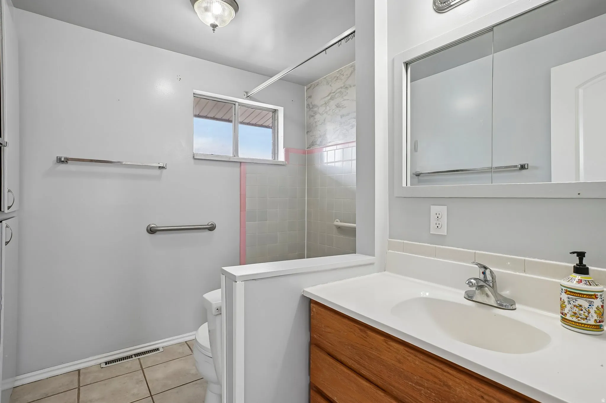 Bathroom featuring a wood-finish vanity with an integrated sink and chrome faucet, tile flooring, and a shower with tiled walls