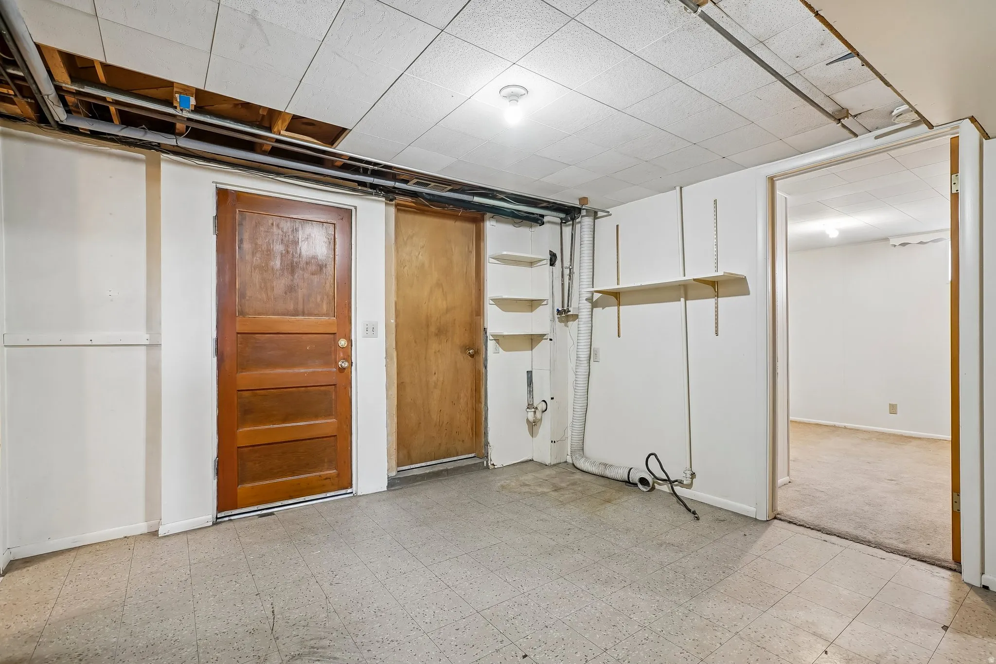 Utility space with paneled wood doors, white painted walls, suspended ceiling tiles, and built-in shelving