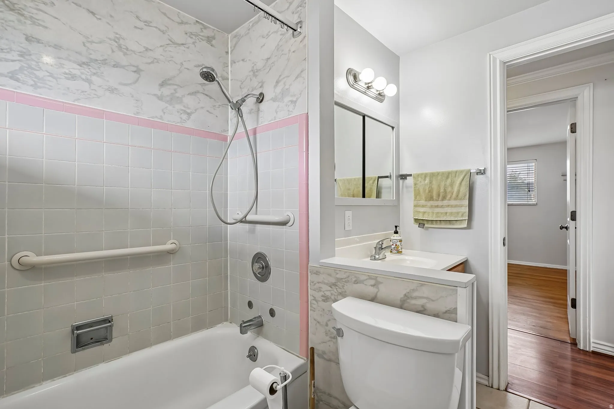 Bathroom featuring a white subway tile tub surround, integrated grab bars, and a handheld showerhead