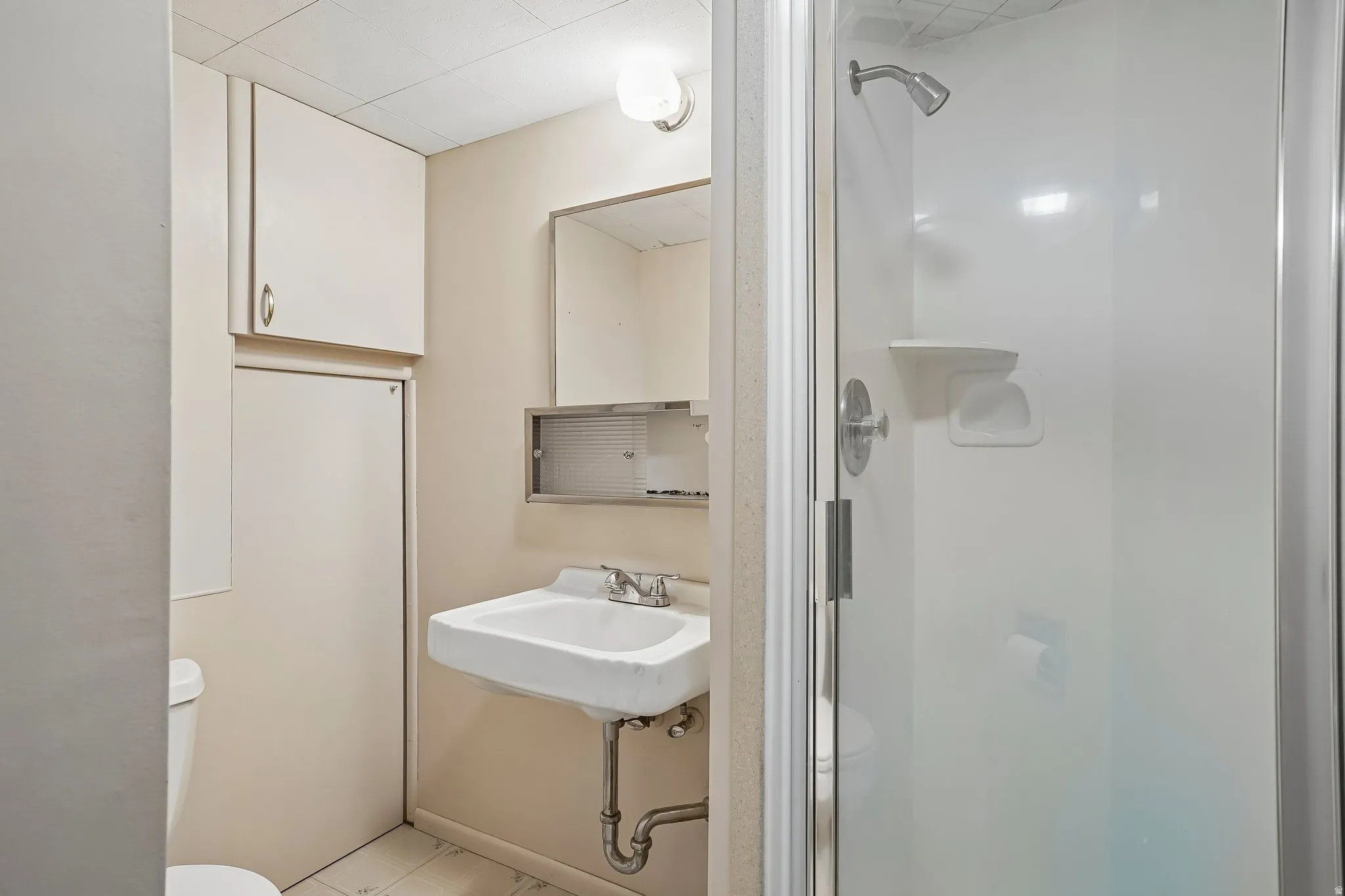 Bathroom with a wall-mounted sink, mirrored medicine cabinet, and a shower enclosure