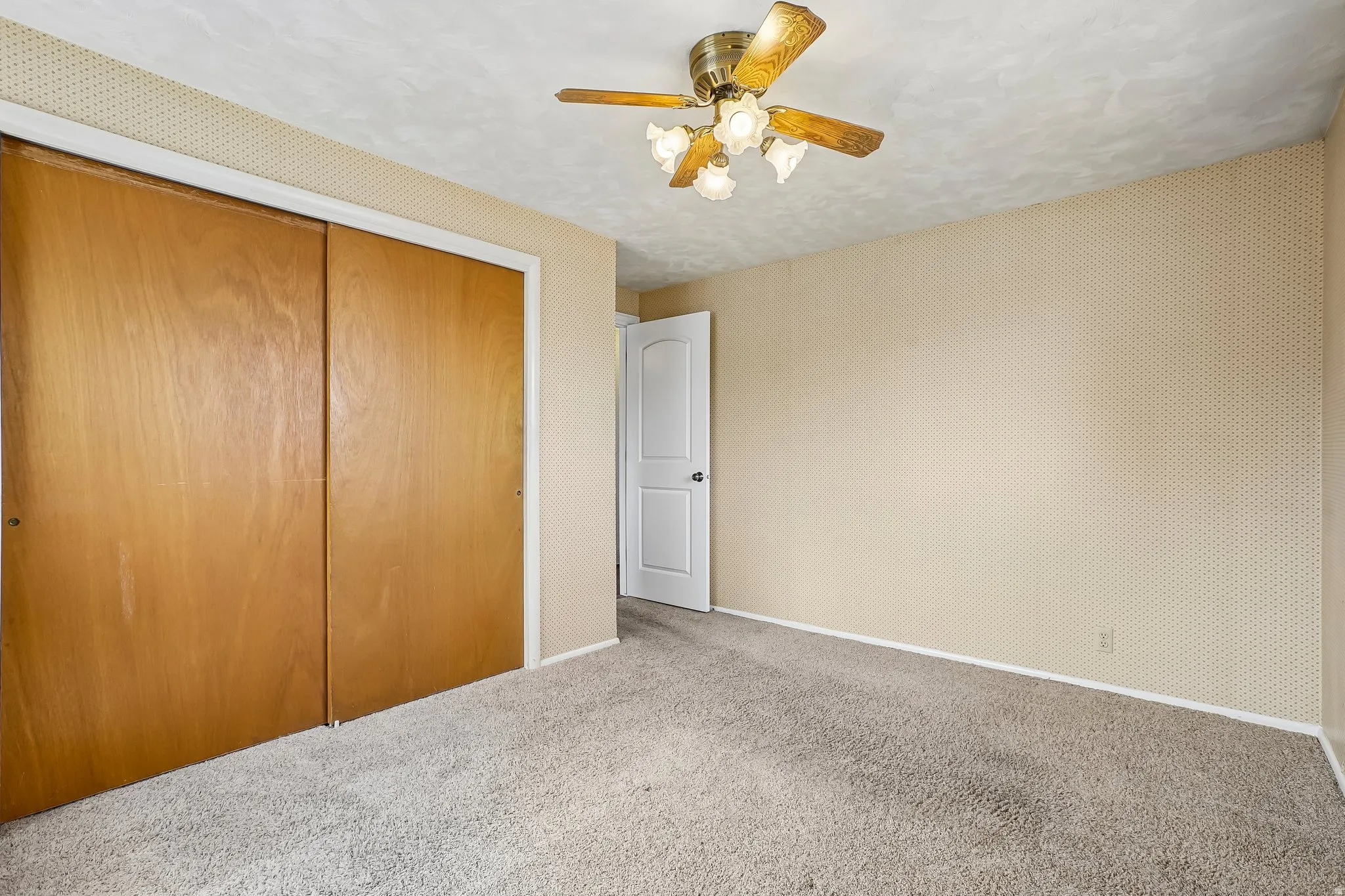 Room featuring wall-to-wall carpeting, light-toned walls with subtle pattern, and a ceiling fan with light fixture