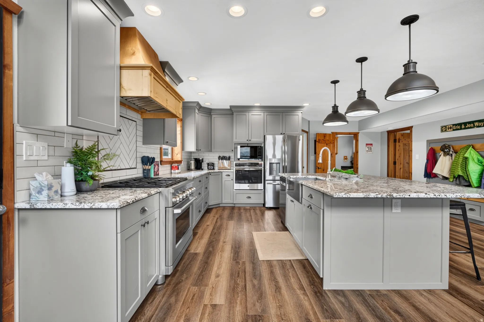 Expansive kitchen featuring wood-finish flooring, light grey cabinetry, stainless steel appliances, a center island with pendant lighting, and a subway tile backsplash