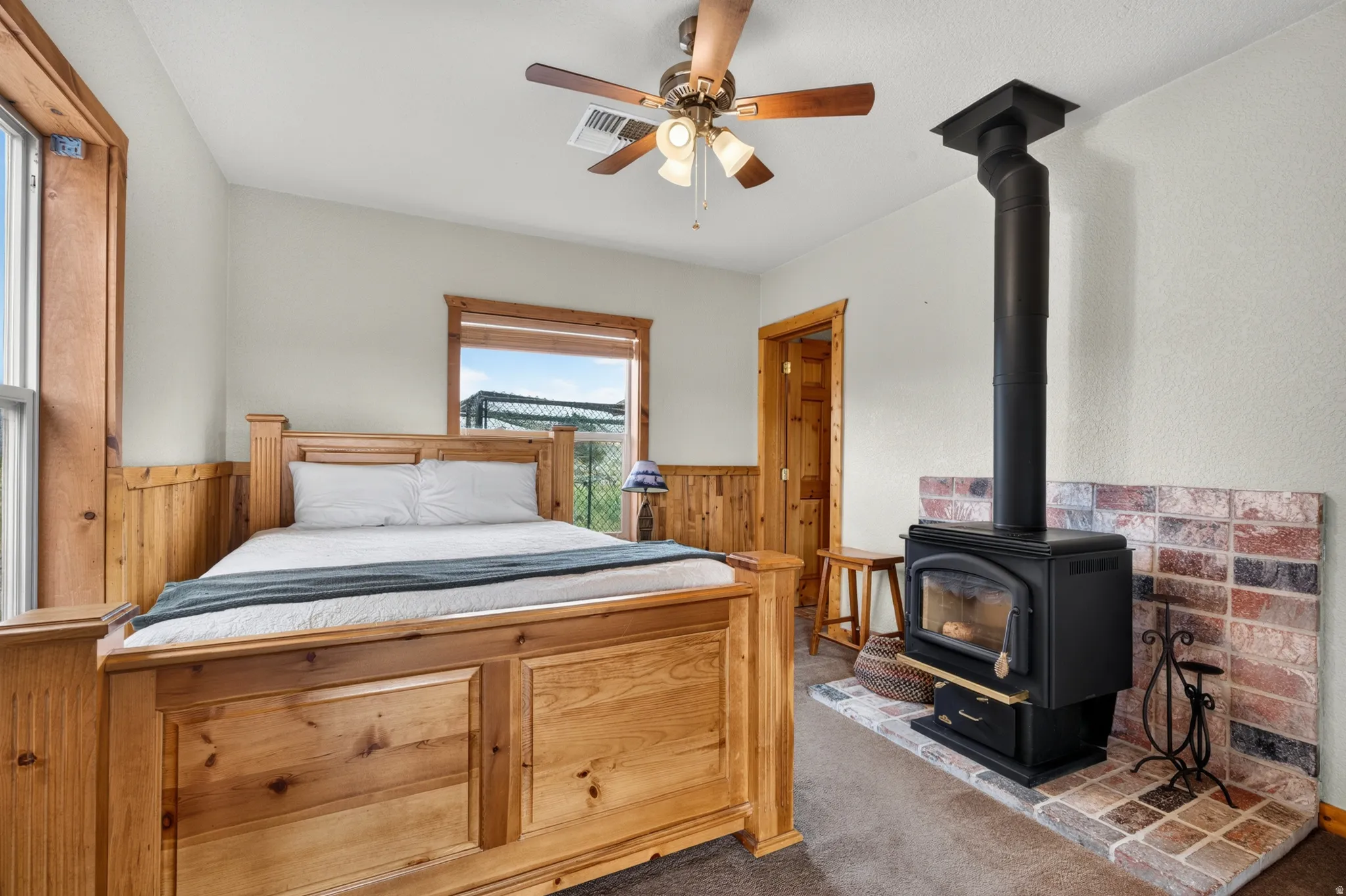 Wood-paneled room featuring a black wood-burning stove with a brick-finish hearth and wall accent, wood-finish window trim, and a ceiling fan with integrated lighting
