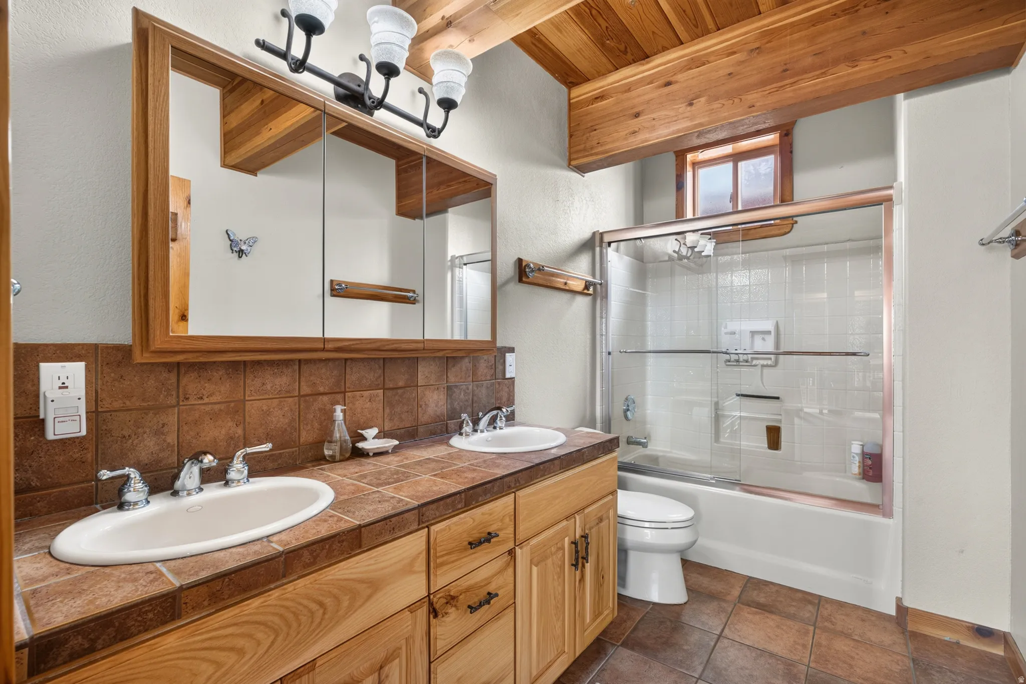 Bathroom featuring a dual vanity with tile countertop, integrated sinks, and wood cabinetry