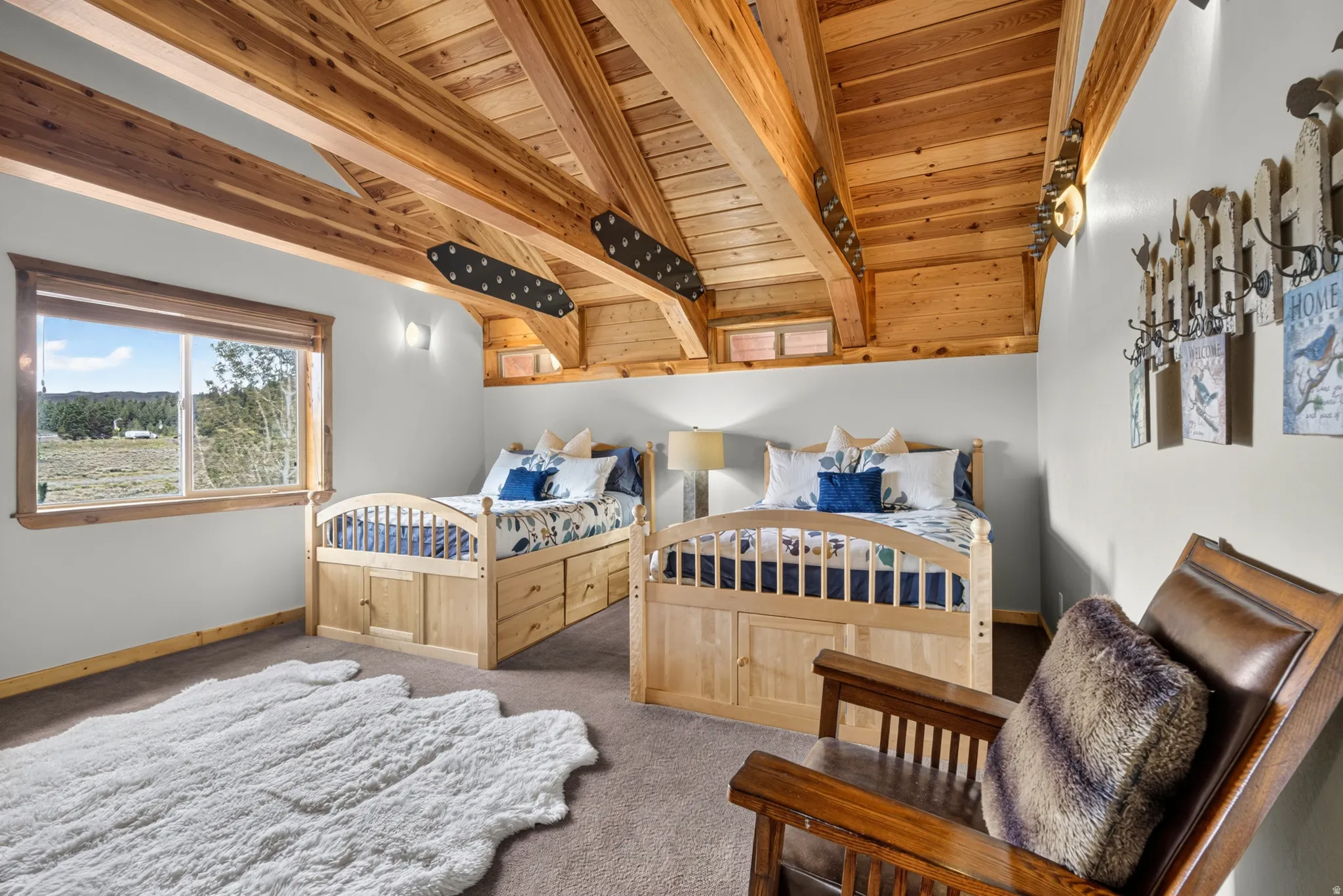 Vaulted wood-paneled ceiling with exposed beams, large picture window with wooden trim, built-in beds with integrated storage, sconce lighting, and carpeted flooring