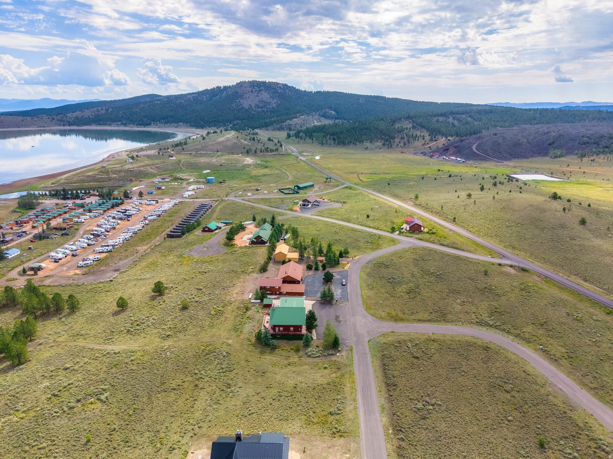 Expansive property featuring a lake, surrounding natural landscape, multiple structures, and a network of unpaved roads