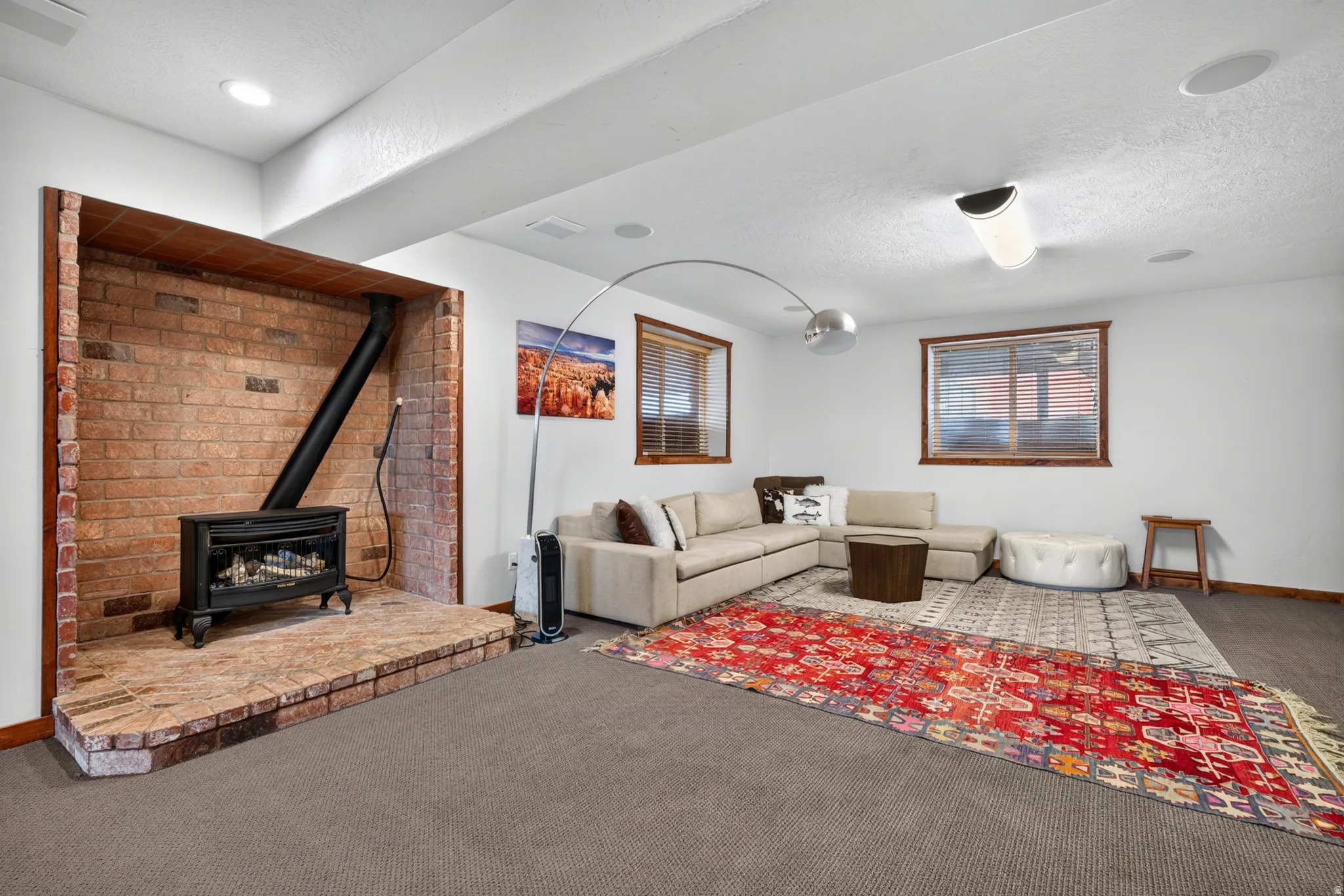 Brick-faced hearth with a freestanding stove, recessed lighting, wood-trim windows, and carpeted flooring