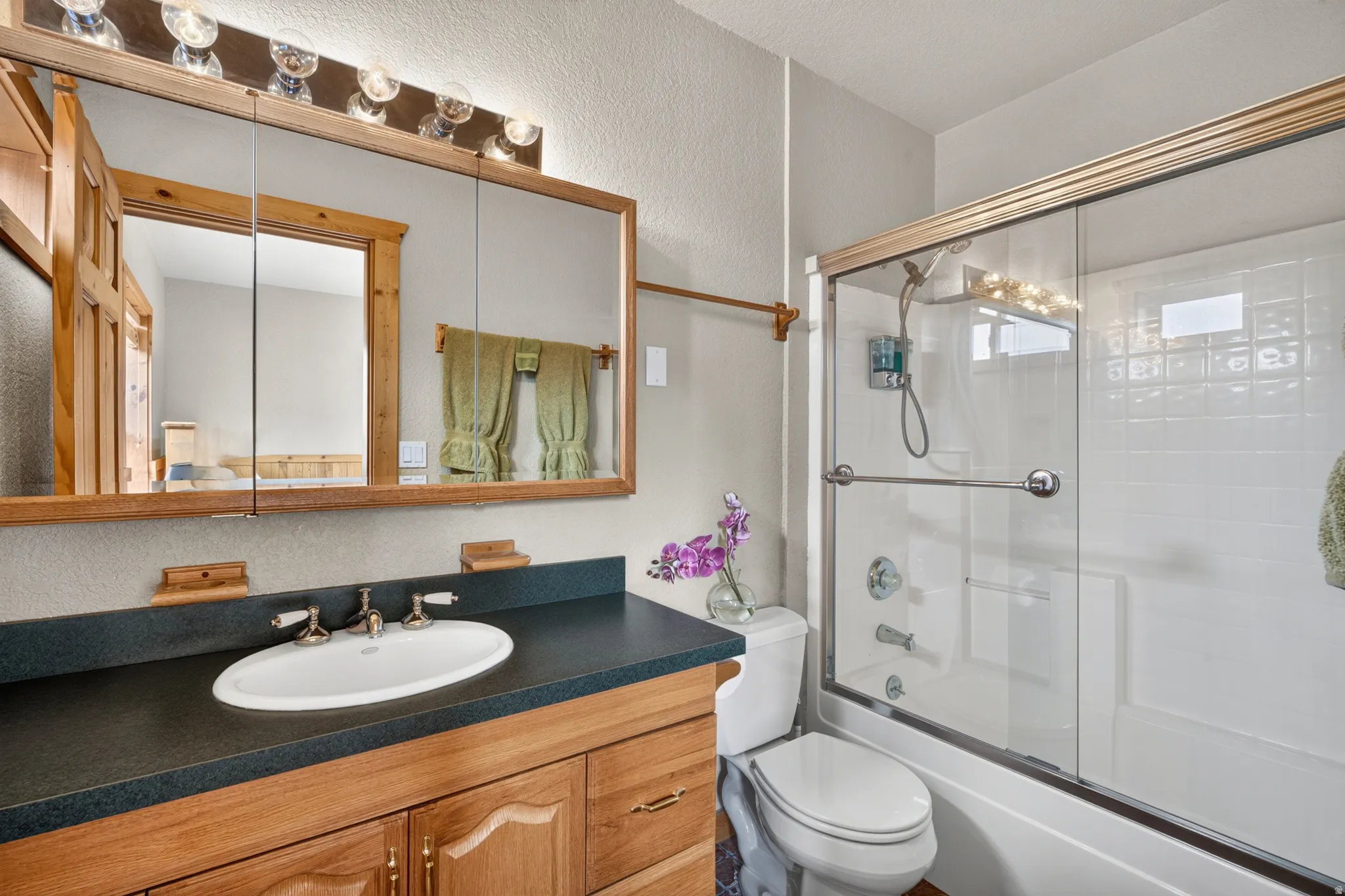 Bathroom featuring a wood-finish vanity with an integrated oval sink and dark countertop, a mirrored medicine cabinet, and overhead vanity lighting