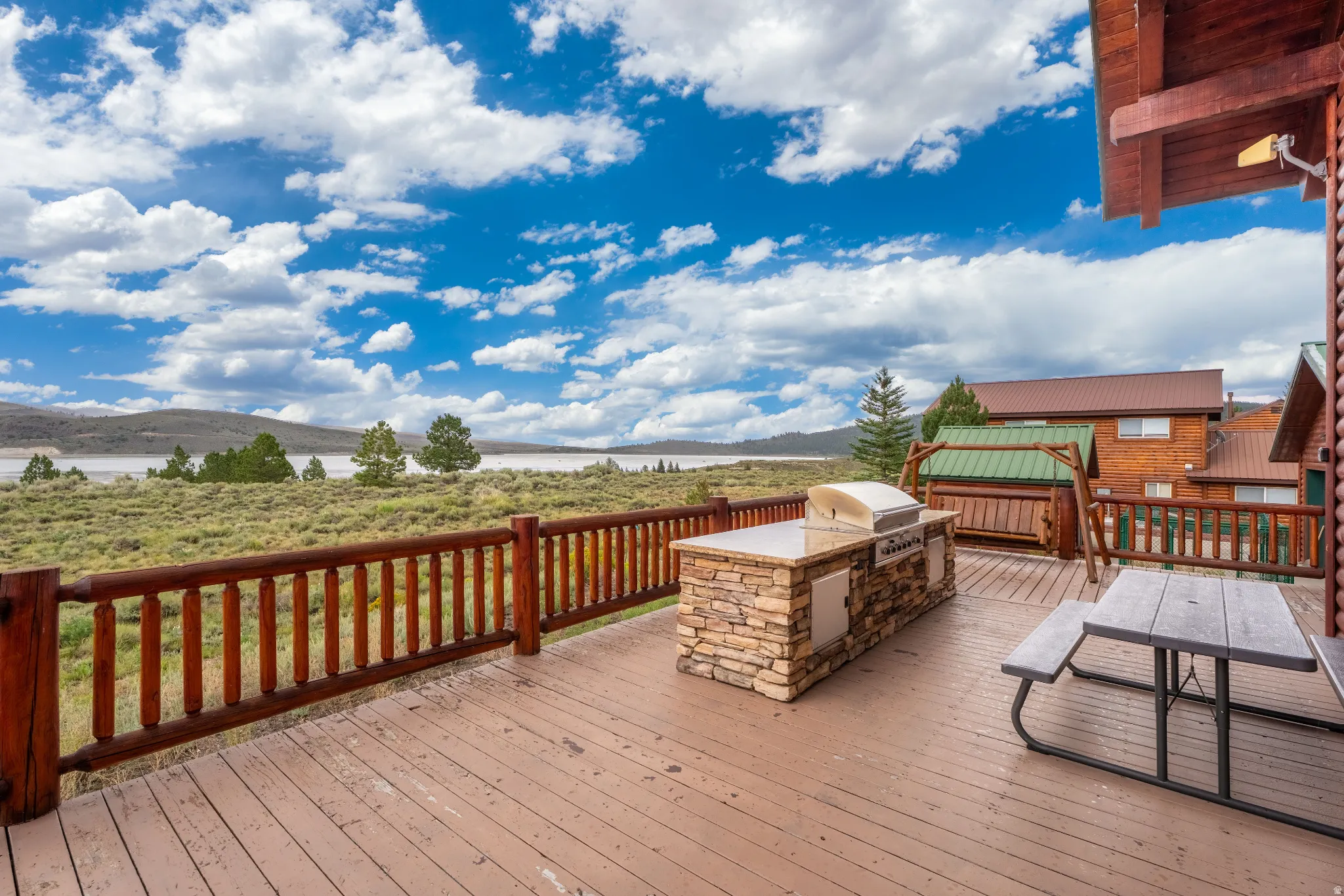 Expansive outdoor deck featuring a built-in stone island with grill, wood railing, and a rustic aesthetic