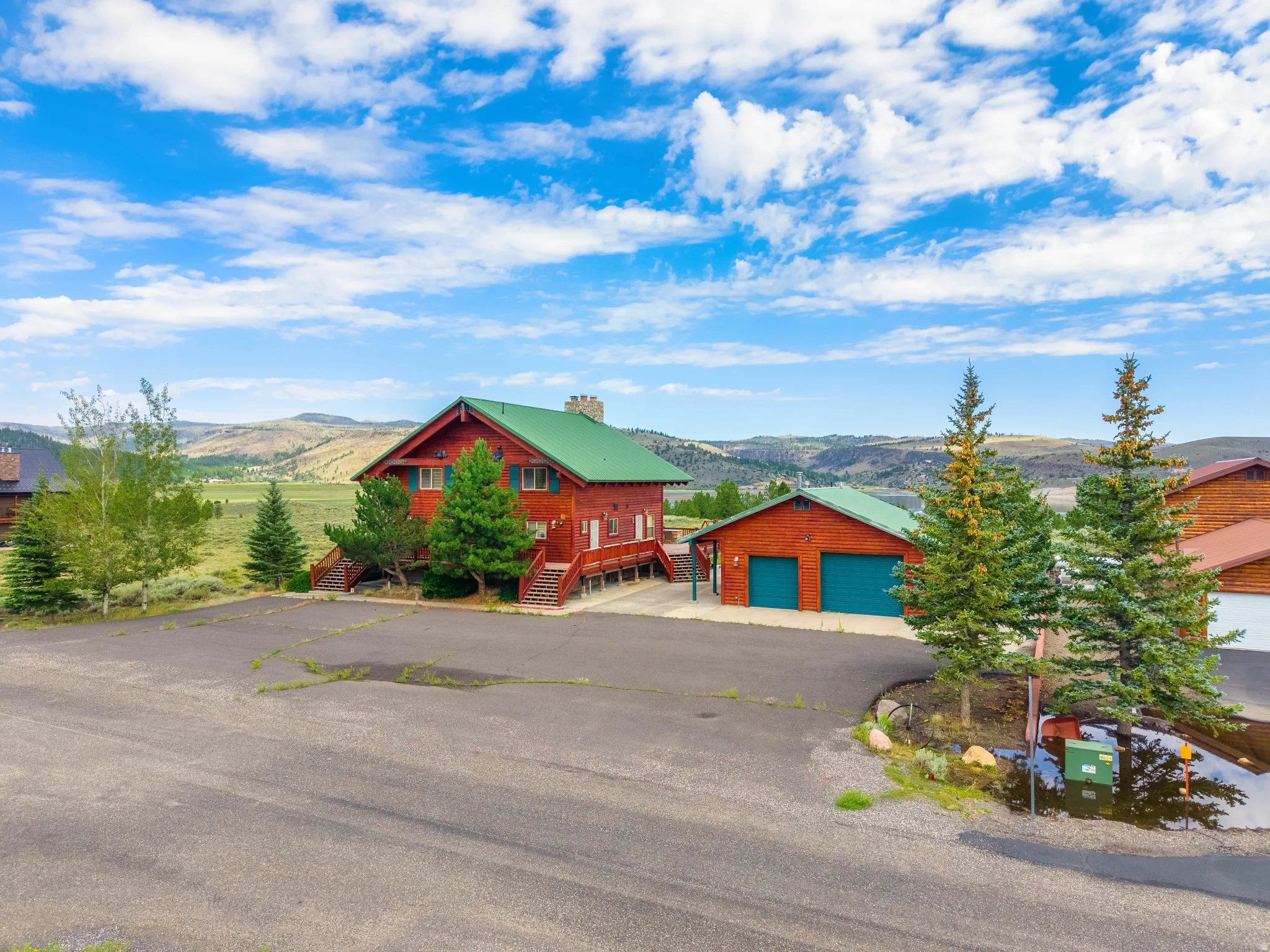Log cabin-style residence featuring a bright green metal roof and a detached two-car garage with matching green doors