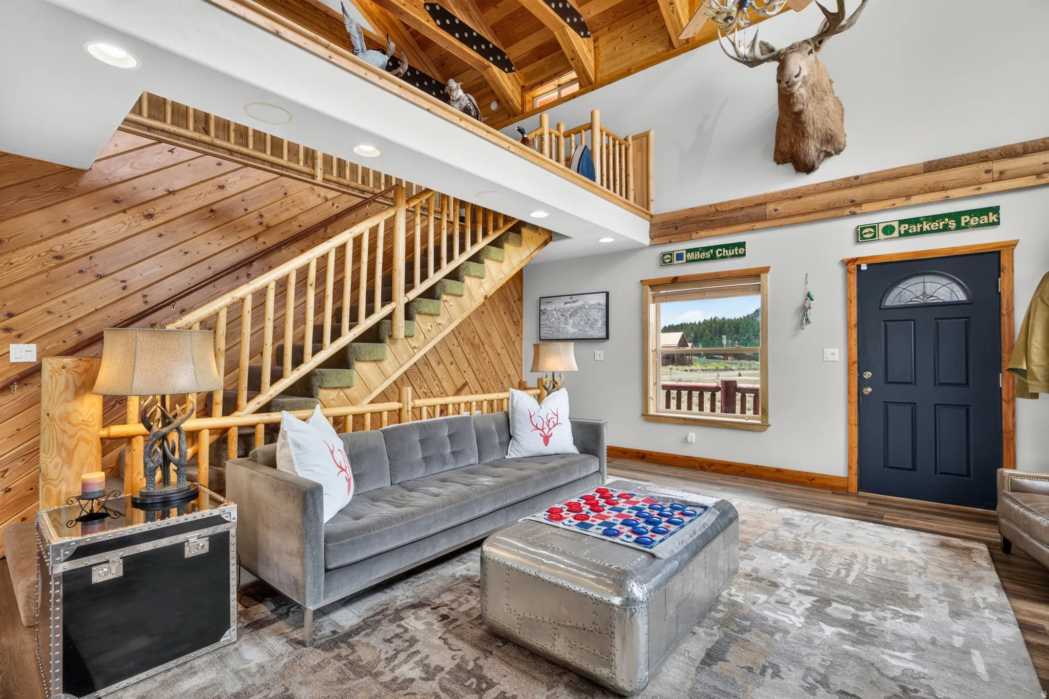 Great room featuring an open-concept design with a wood-paneled accent wall, natural wood staircase, a lofted area, and a dark-paneled entry door