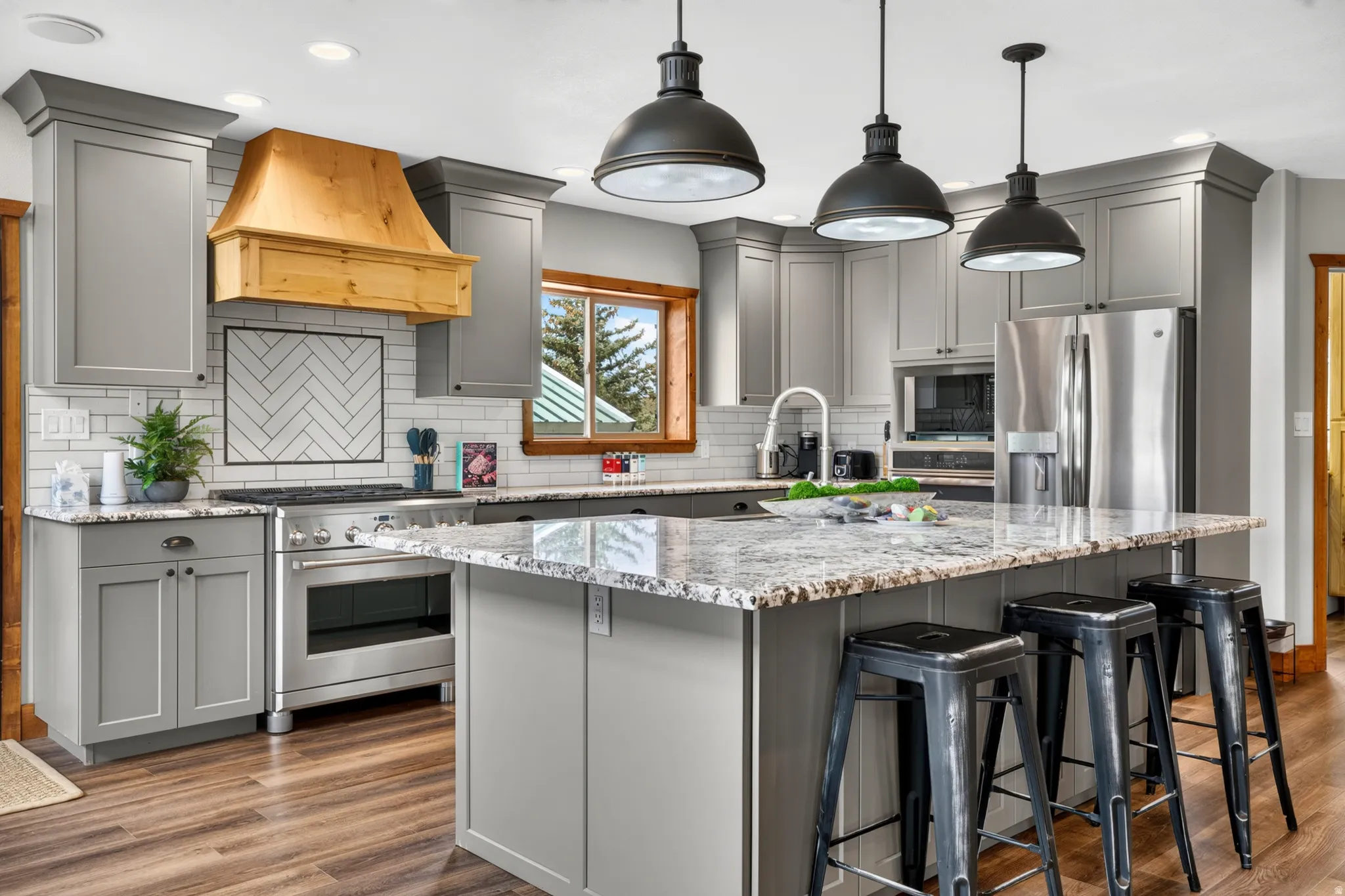 Kitchen featuring light gray cabinetry, a wood-finish range hood, stainless steel appliances, and granite countertops