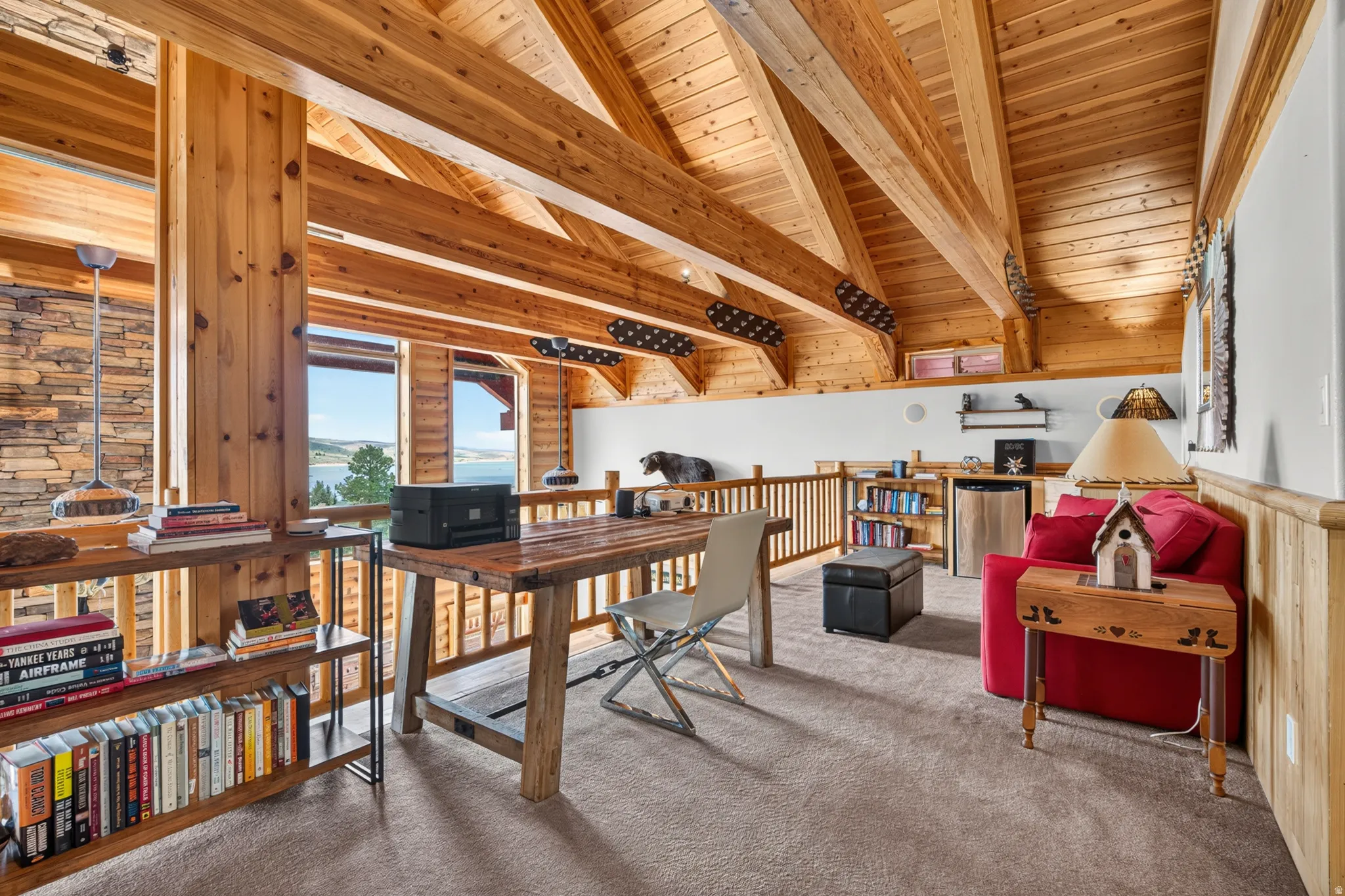 Loft space featuring exposed wood beams and ceiling, a built-in wood railing, and a window offering a distant water view