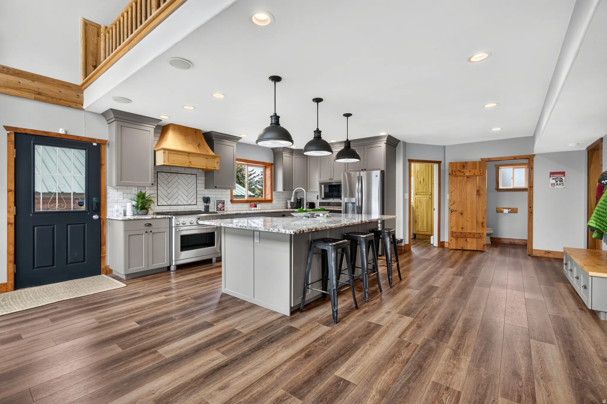 Open-concept kitchen featuring gray cabinetry, stainless steel appliances, a wood-finish hood, and a central island with bar seating