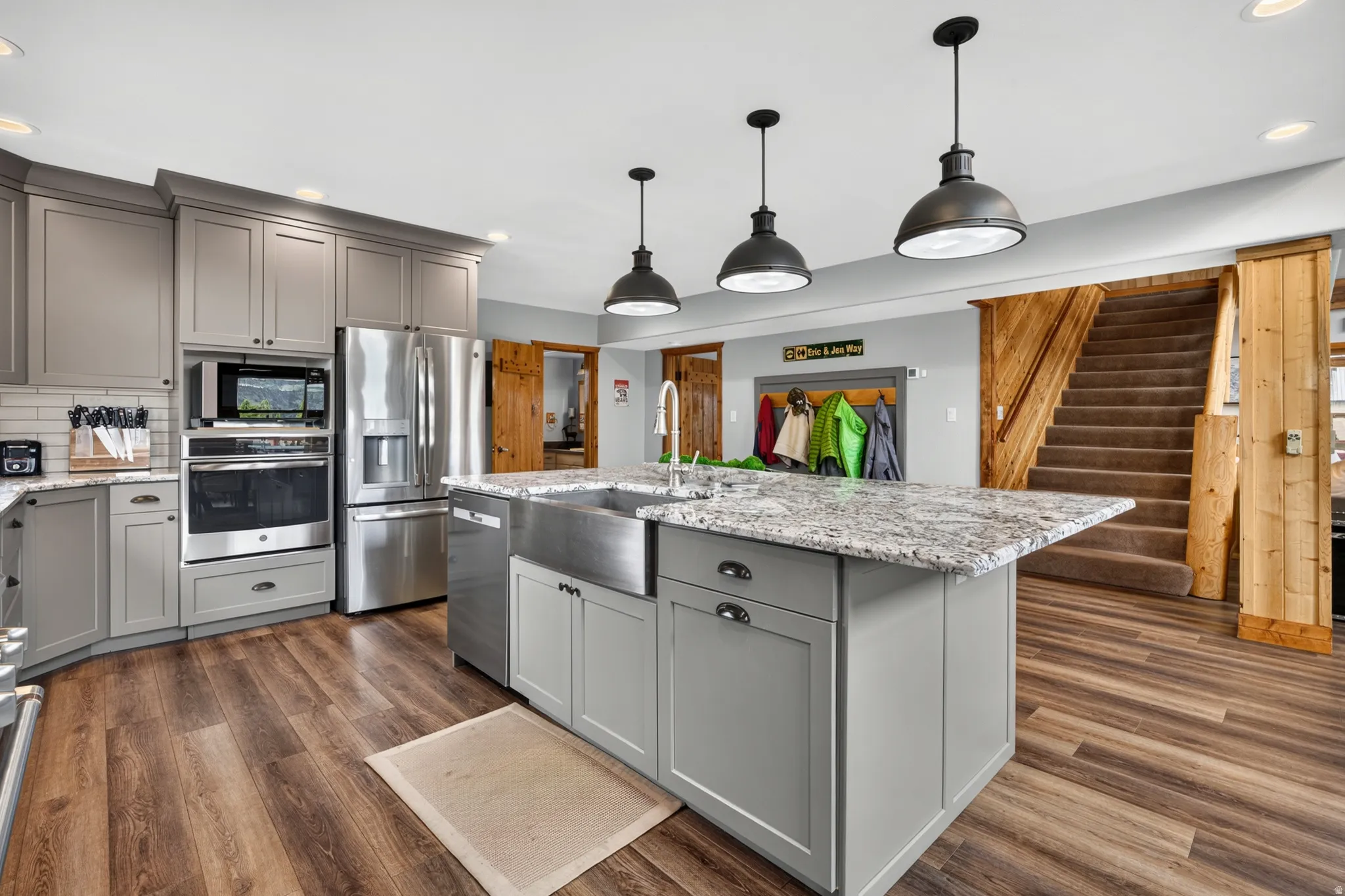 Modern kitchen featuring a stainless steel farmhouse sink, gray cabinetry, granite countertops, and wood-finish flooring