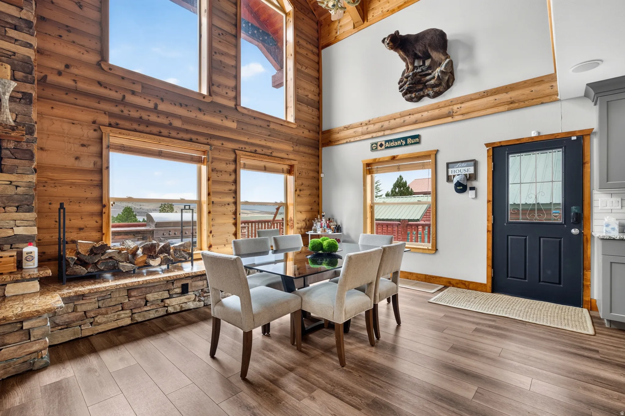 Spacious dining area featuring wood-finish flooring, a stone-clad fireplace with a granite hearth, and large windows offering exterior views