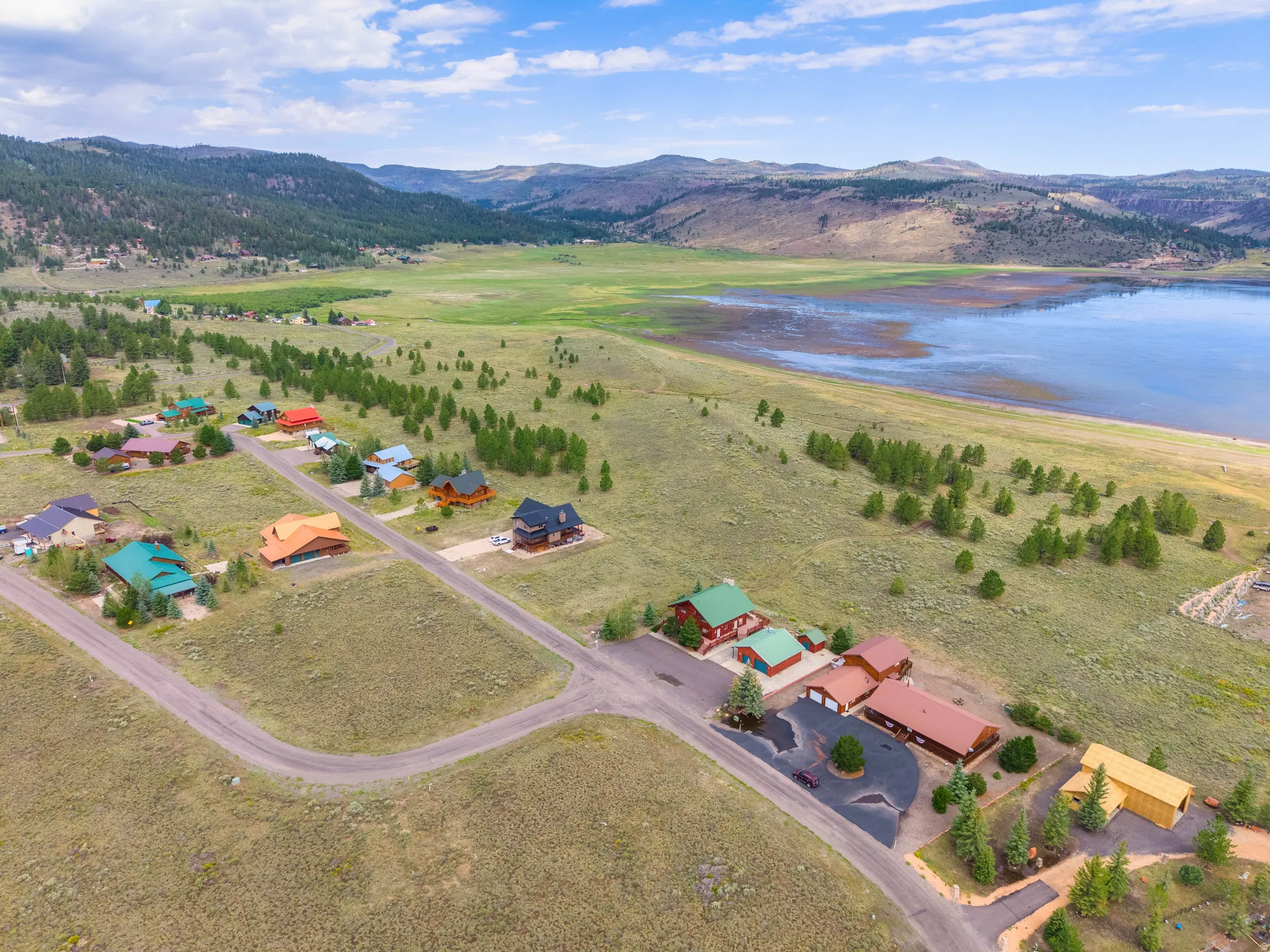 Aerial perspective showcasing properties situated along a large body of water, with surrounding hills and scattered evergreen trees