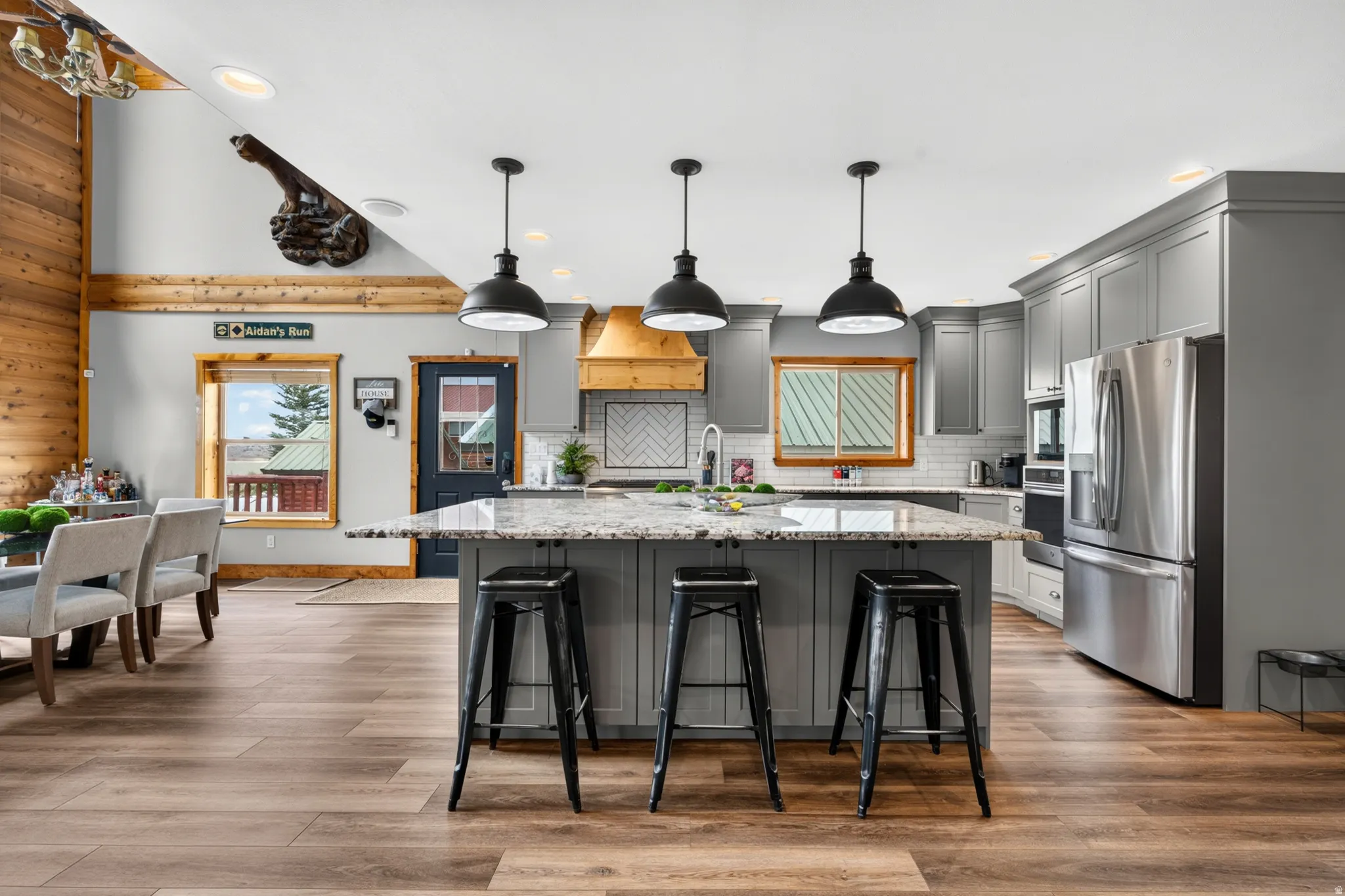 Open-concept kitchen with a large island featuring a light-toned countertop, gray cabinetry, stainless steel appliances, and wood-finish flooring