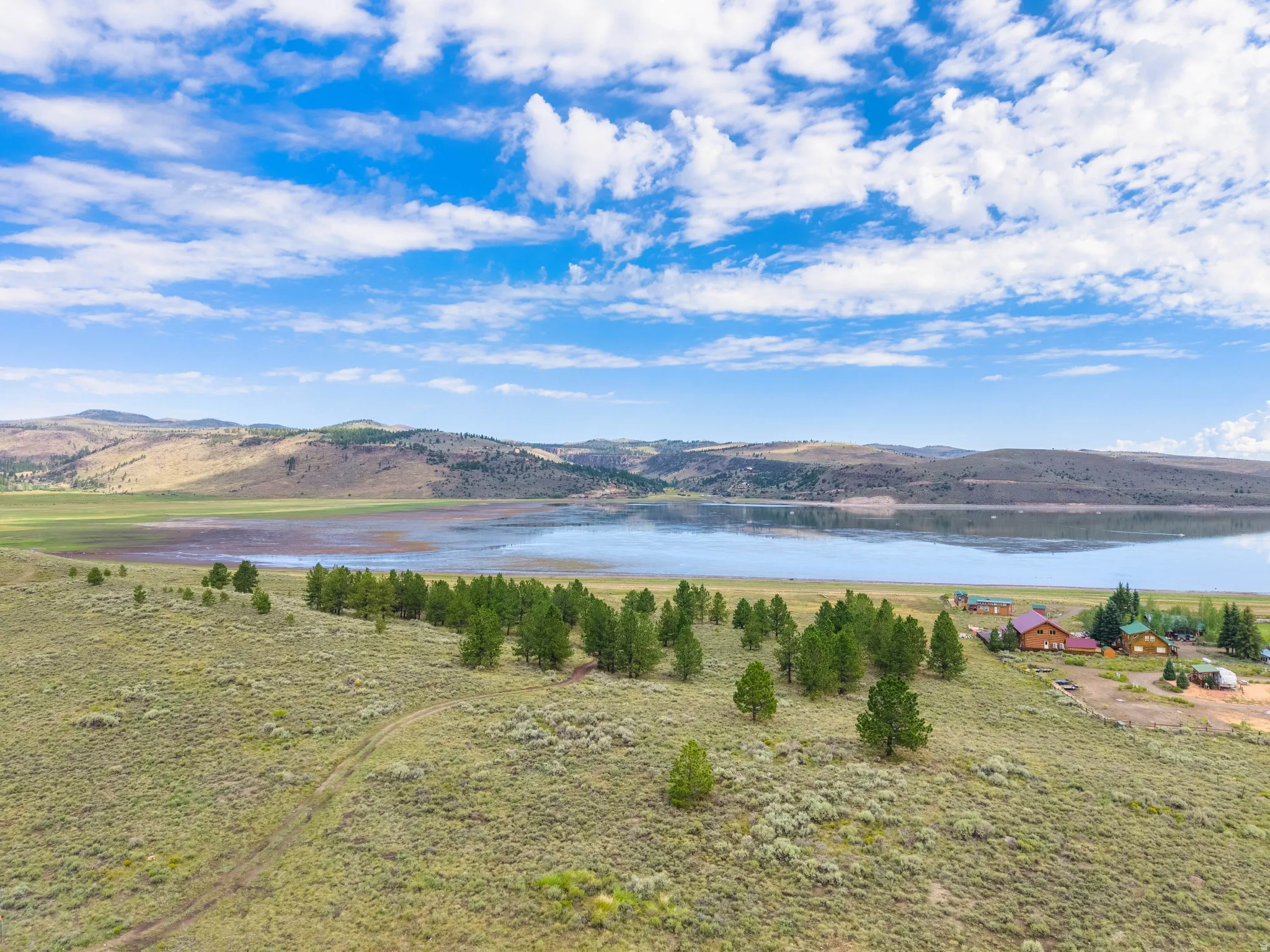 Expansive landscape featuring a large body of water, distant hills, natural vegetation, and a cluster of structures