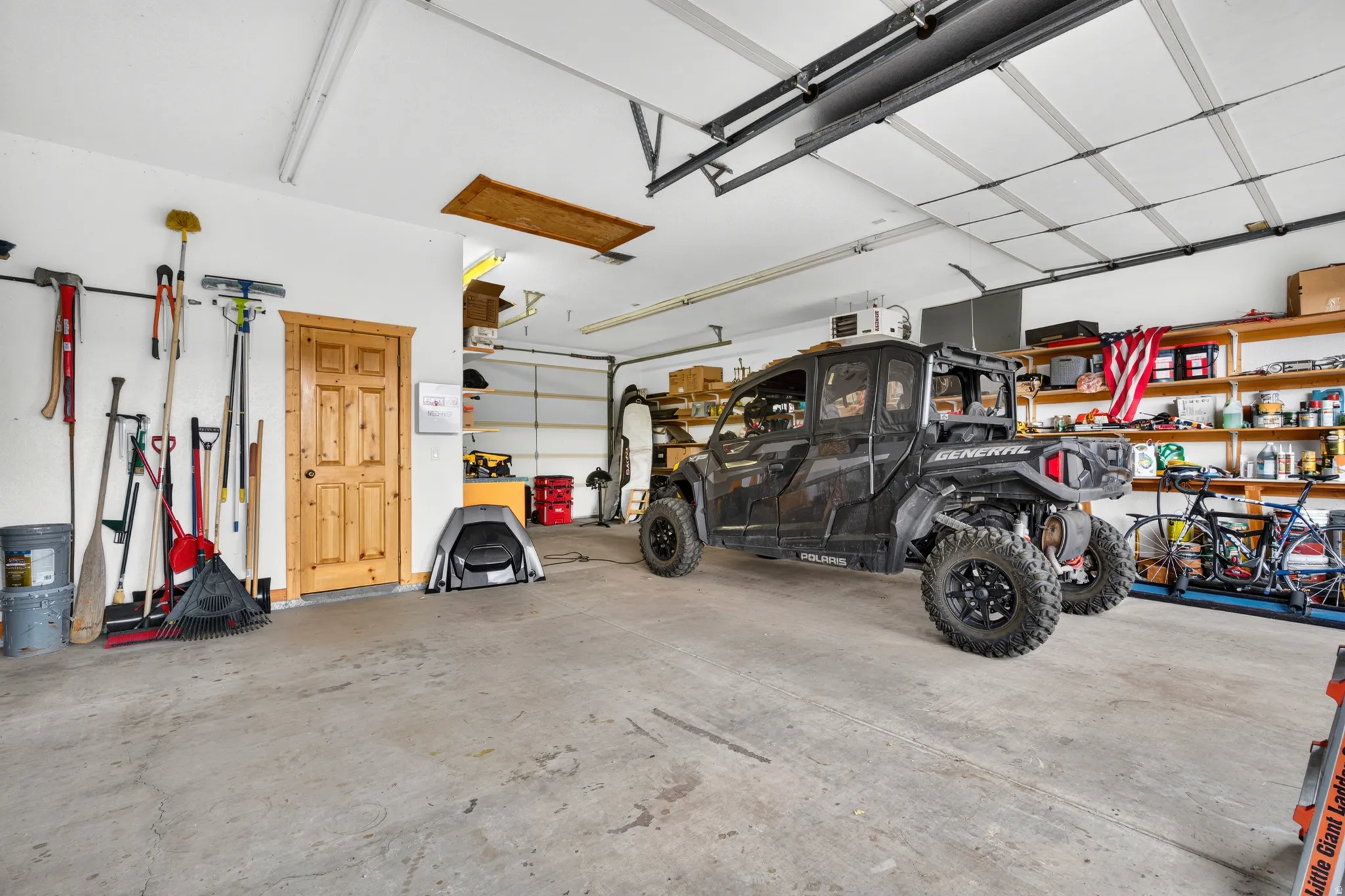 Spacious garage featuring a concrete floor, overhead lighting, an interior wood-panel door, and a built-in shelving system