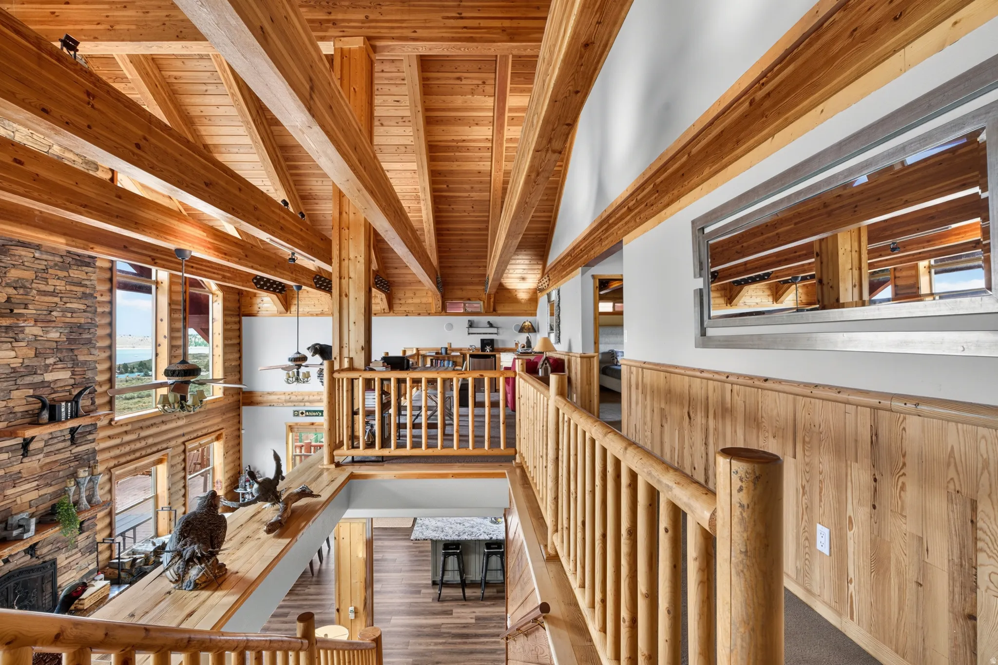 Vaulted ceilings with exposed wood beams throughout, stone-faced fireplace, natural wood log railing, and wood-finish wall paneling