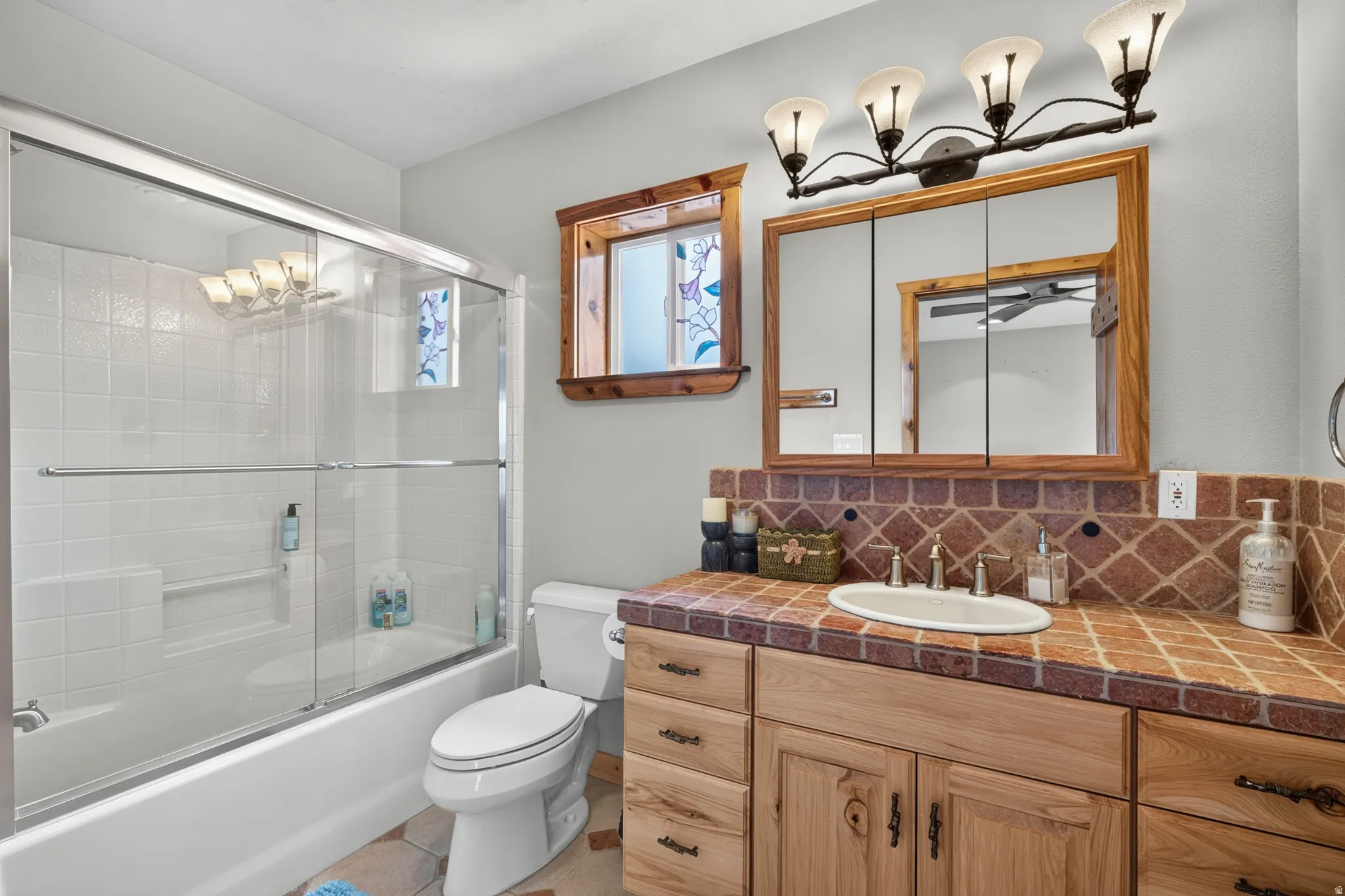 Bathroom featuring a tile countertop with an undermount sink, wood vanity cabinetry, a framed medicine cabinet, and a bathtub with a sliding glass enclosure