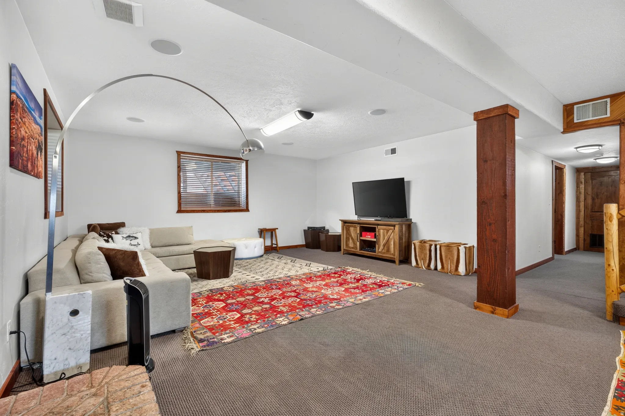 Spacious lower-level entertainment area featuring recessed lighting, a wooden window frame, an exposed wood column, and built-in ceiling speakers