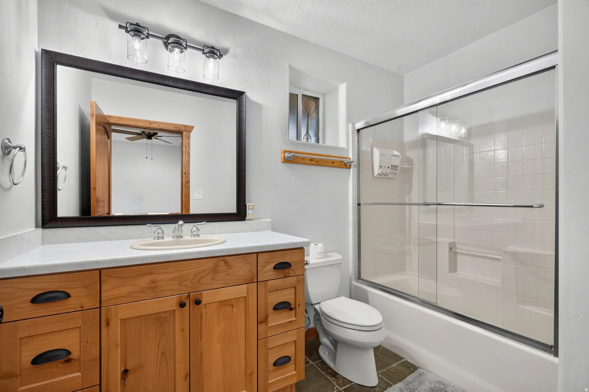 Bathroom featuring a wood-finish vanity with a light-colored countertop, an undermount sink, and a framed mirror