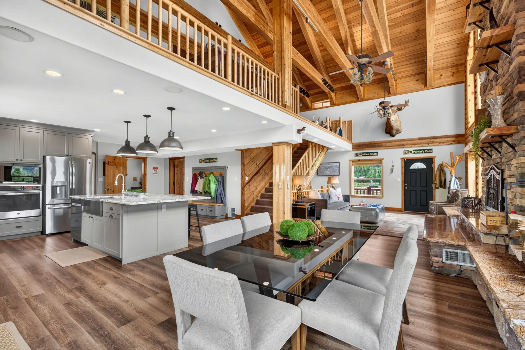 Open-concept living space featuring vaulted wood-beam ceilings, a stone fireplace, and wood-finish flooring
