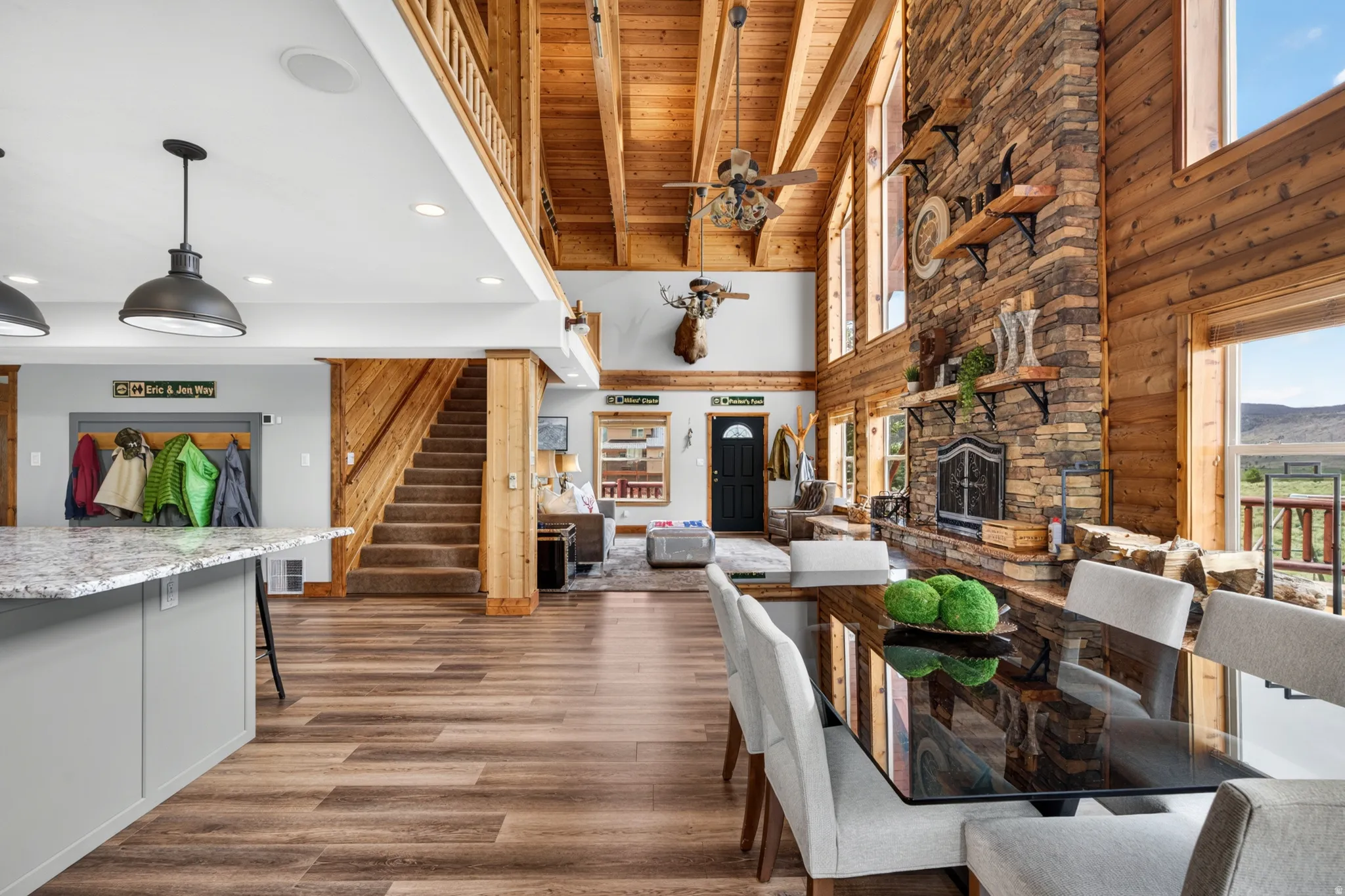 Spacious open-concept living area featuring a floor-to-ceiling stone fireplace, high vaulted wood-paneled ceilings, and wood-finish flooring