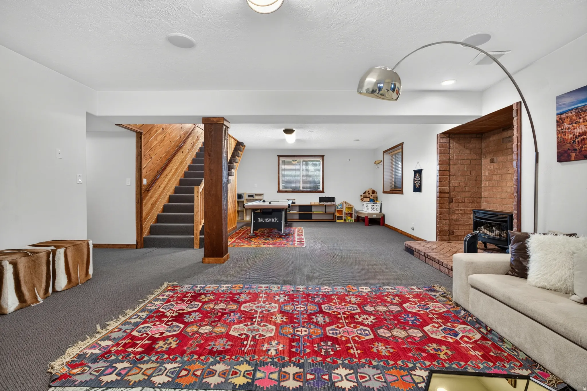 Spacious lower-level room featuring gray carpeting, a brick-surround fireplace with a hearth, and built-in wood shelving