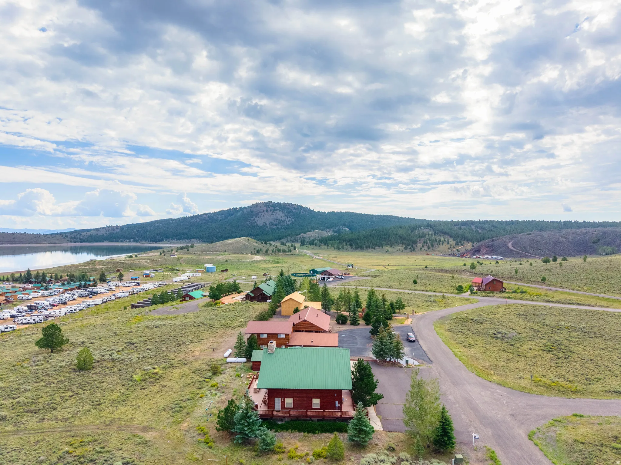 Expansive property featuring multiple structures with green and red roofs, a large gravel parking area, and a paved road