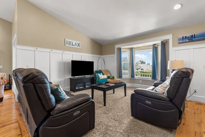 Spacious living room featuring dual power reclining leather chairs, wood-finish flooring, and built-in media cabinetry with integrated entertainment center