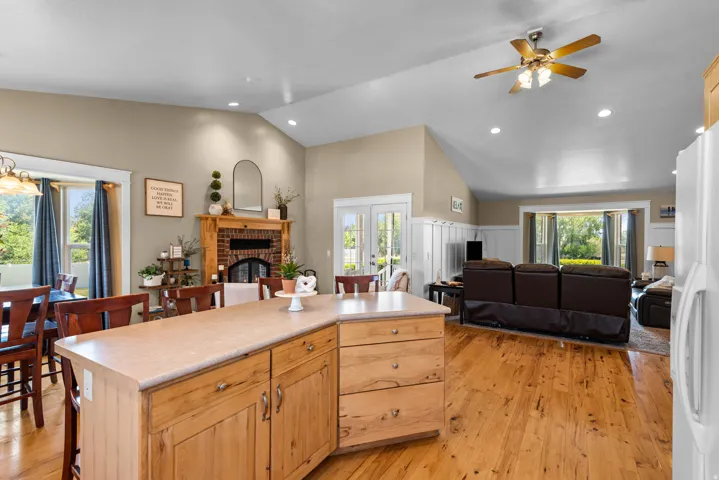 Open-concept living area featuring vaulted ceilings, wood-finish flooring, a brick fireplace, and built-in paneling