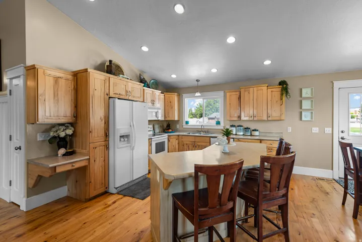 Open-concept kitchen featuring wood-finish flooring, light wood cabinetry, recessed lighting, a kitchen island with seating, and a window above the sink