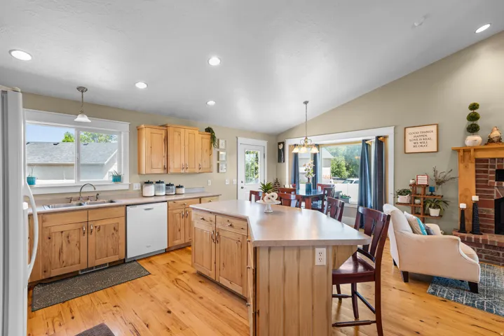Open-concept kitchen and dining area featuring warm wood cabinetry with shaker-style doors, white apron-front sink, wood-finish flooring throughout, and a large center island with seating
