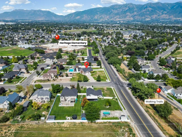 Aerial view showcasing this residential property situated on an expansive lot with mature landscaping, direct access via paved roadway, and proximity to Heritage Elementary School