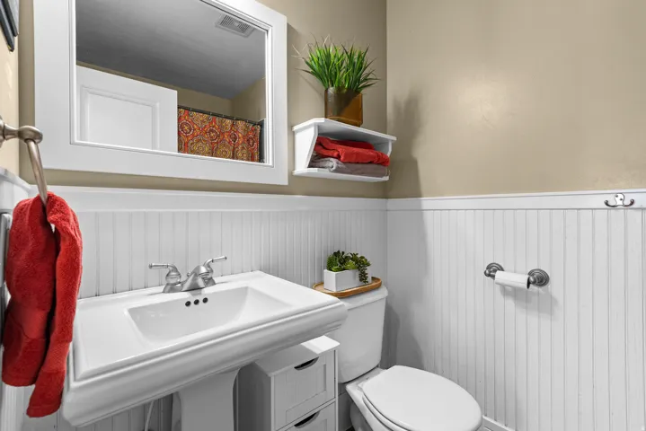Efficiently designed half bath featuring a pedestal sink with chrome faucet and fixtures, white subway tile wainscoting, toilet with wall-mounted supply line, and a recessed medicine cabinet with mirror