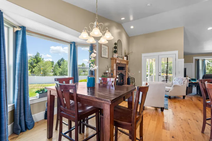Bay window with outdoor scenery, vaulted ceilings, wood-finish flooring, a brick fireplace, and double French doors